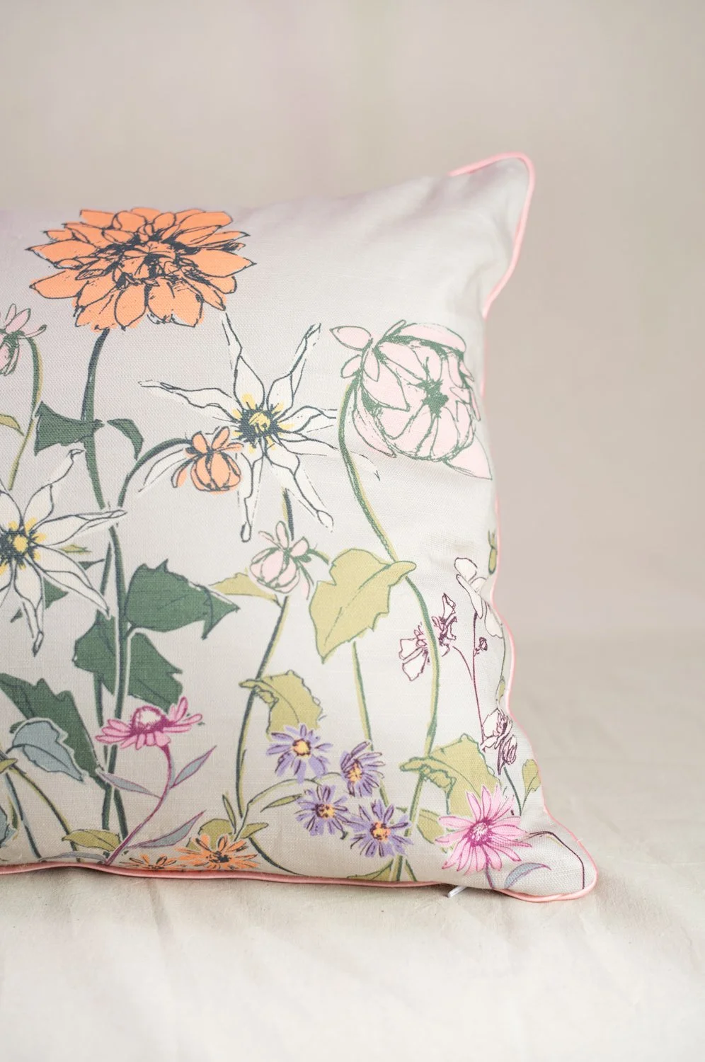 Decorative pillow with a floral pattern featuring various colored flowers and green leaves, with pink piping along the edges.
