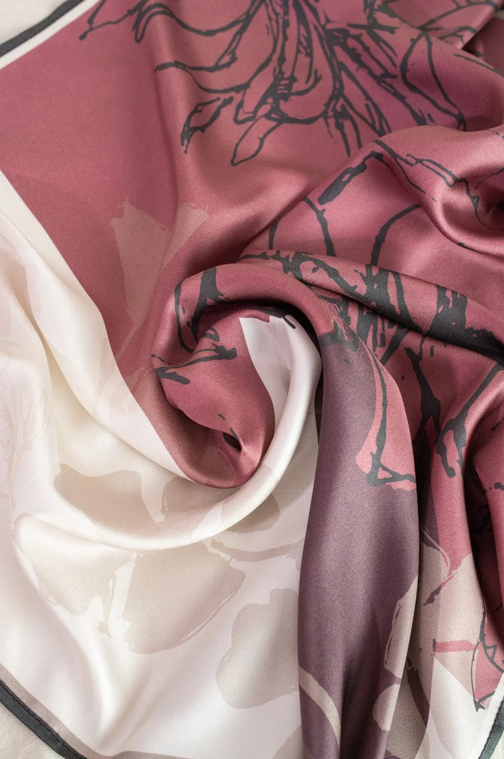 Close-up of a pink, purple, and cream silk scarf with floral and abstract patterns, showing soft folds and sheen.