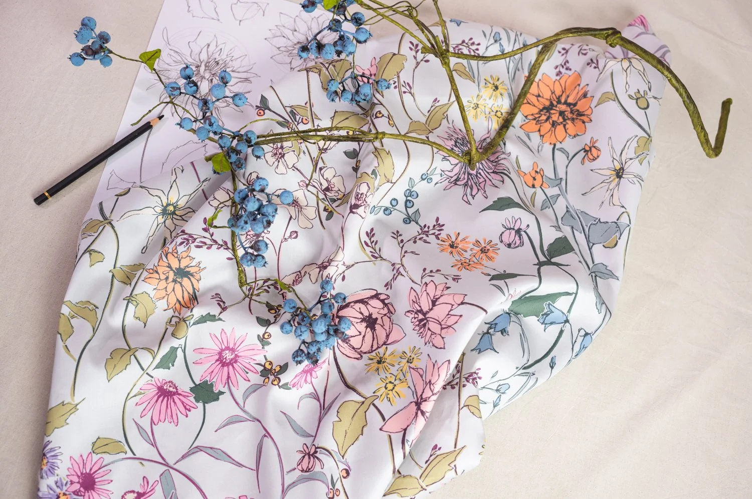 A colorful floral patterned fabric with blue berries and green vine stems laid on a light surface, with a black pen to the side.