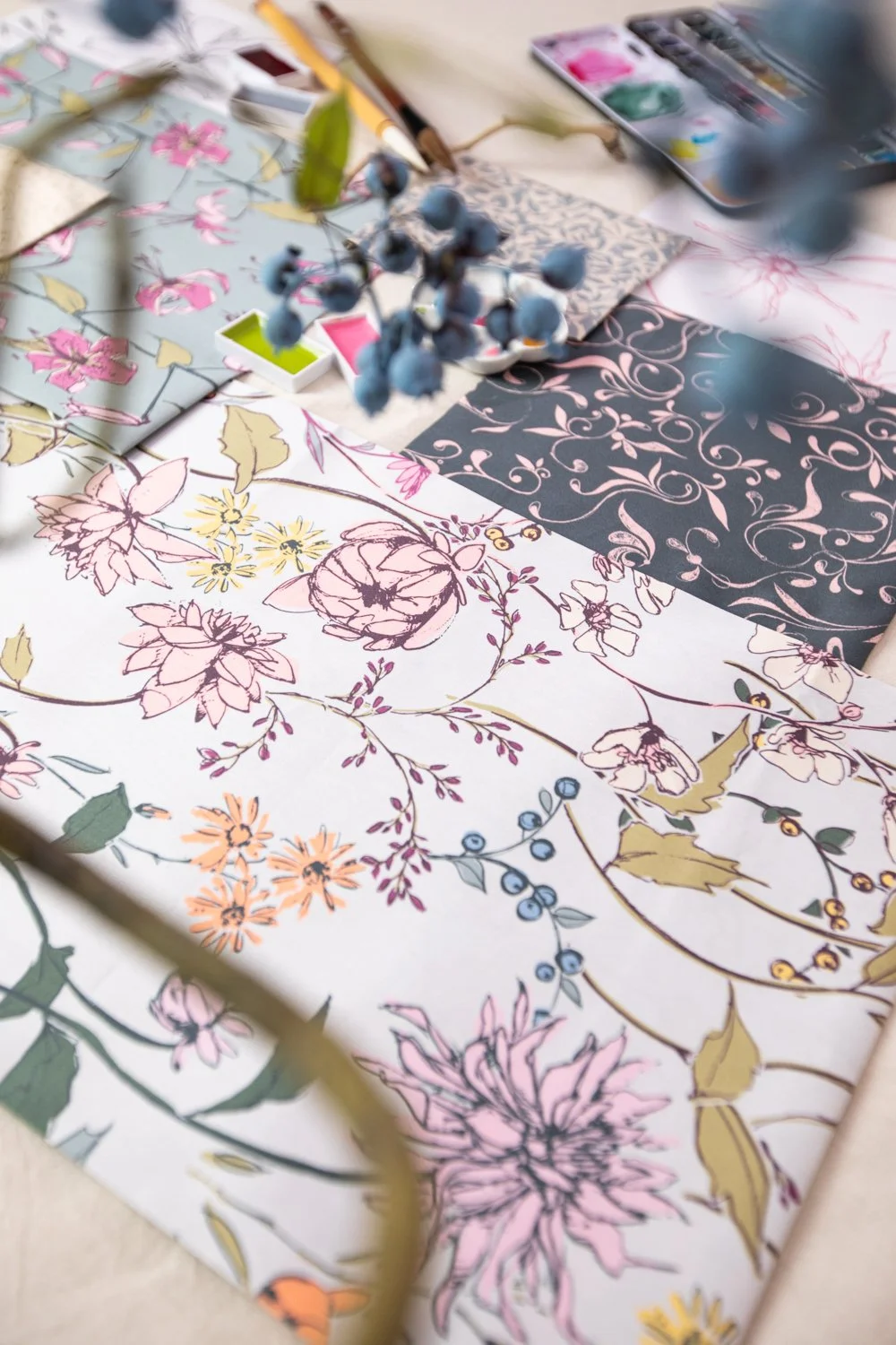 A workspace with floral patterned papers, watercolor paints, and paintbrushes, suggesting an art or craft project in progress.