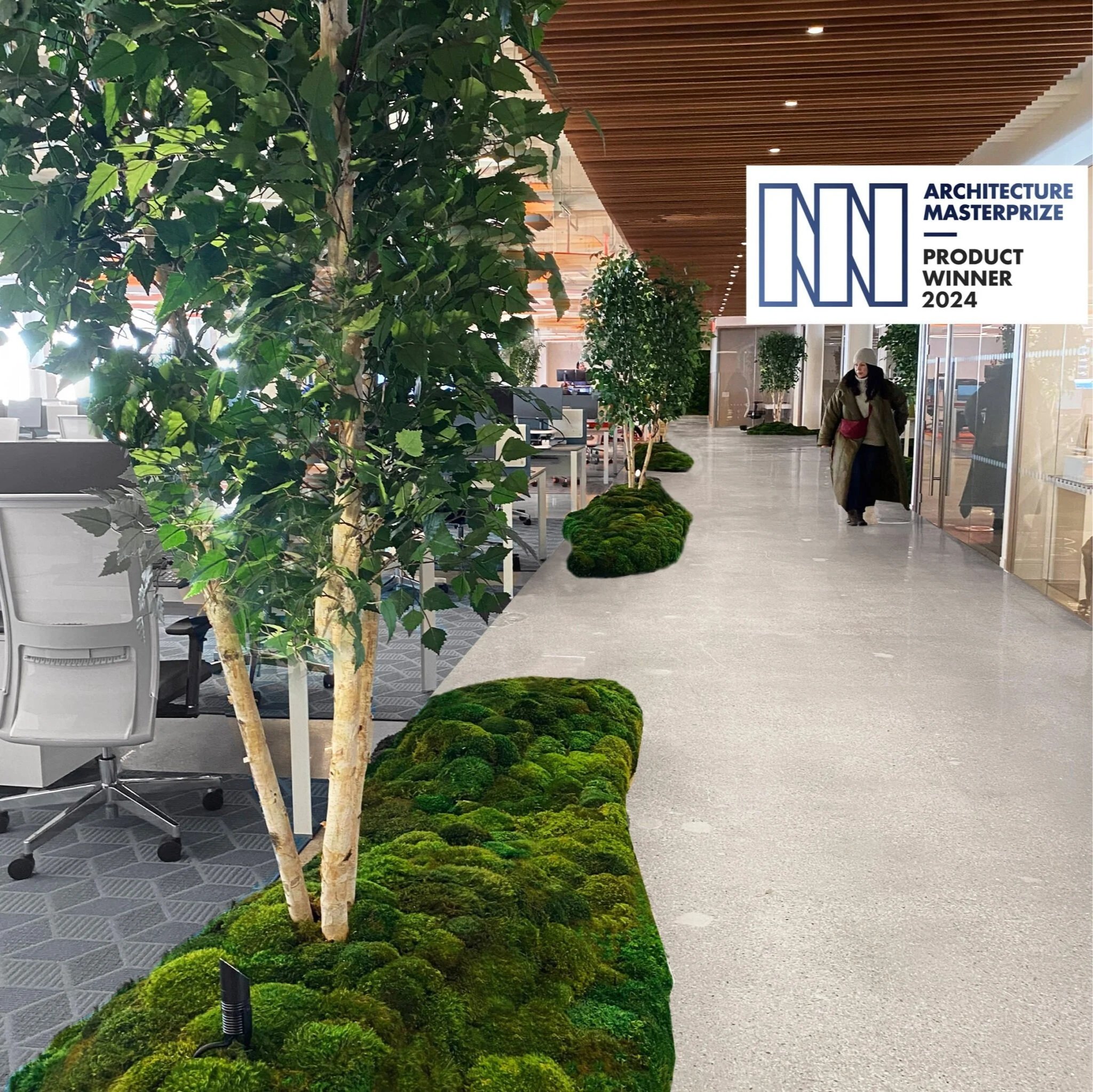 Modern office interior with green plants and moss decor along the walkway, featuring a person walking past glass doors, and an award badge for Architecture MasterPrize 2024 in the top right corner.