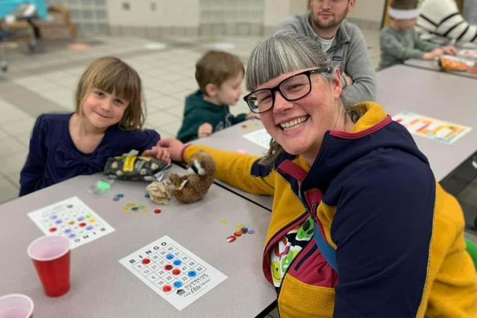 A parent and student seated at a table smile with their Bingo cards.