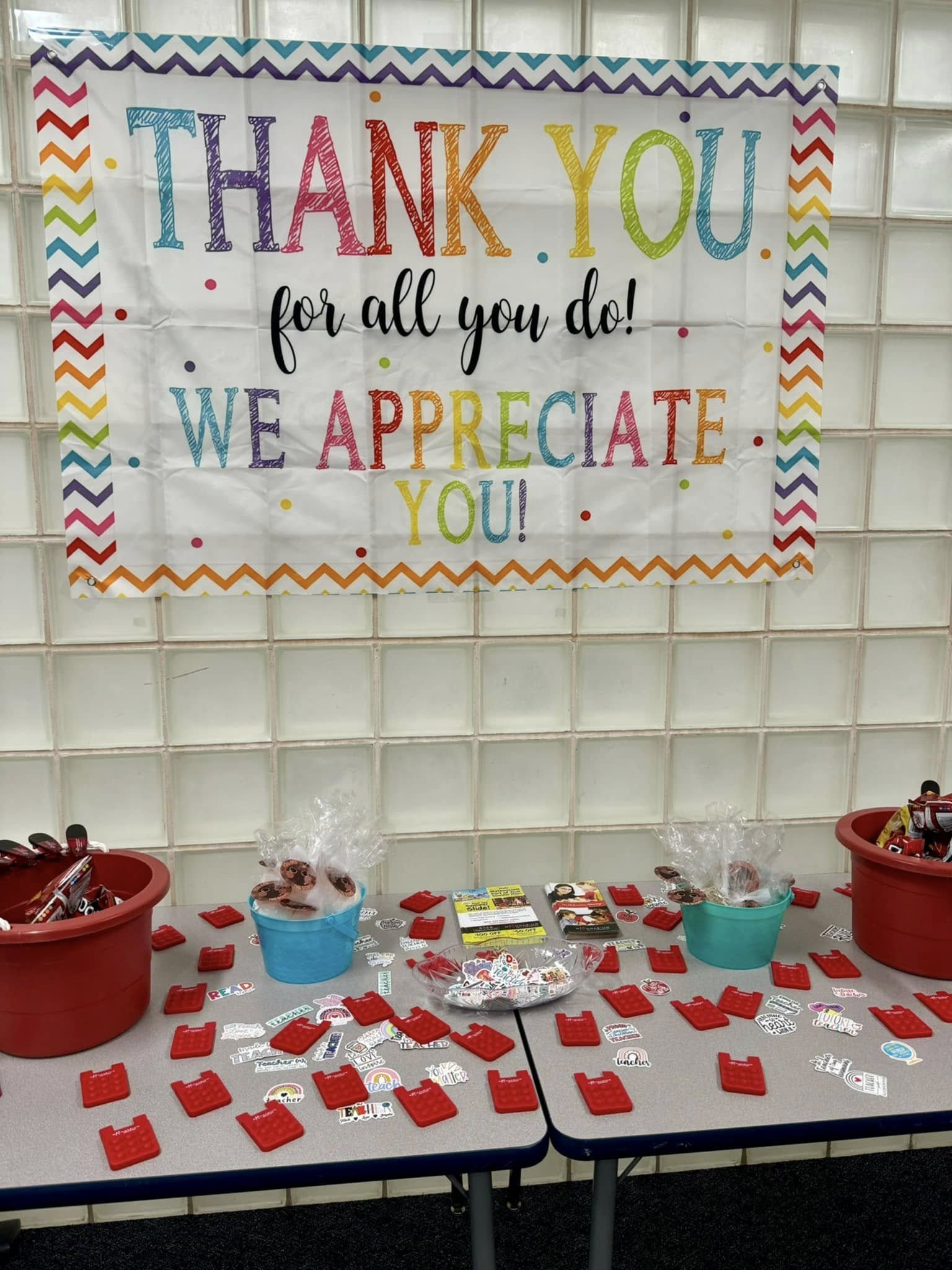 A rainbow colored banner proclaiming "Thank you for all you do! We appreciate you!" hangs above a table with goodies.