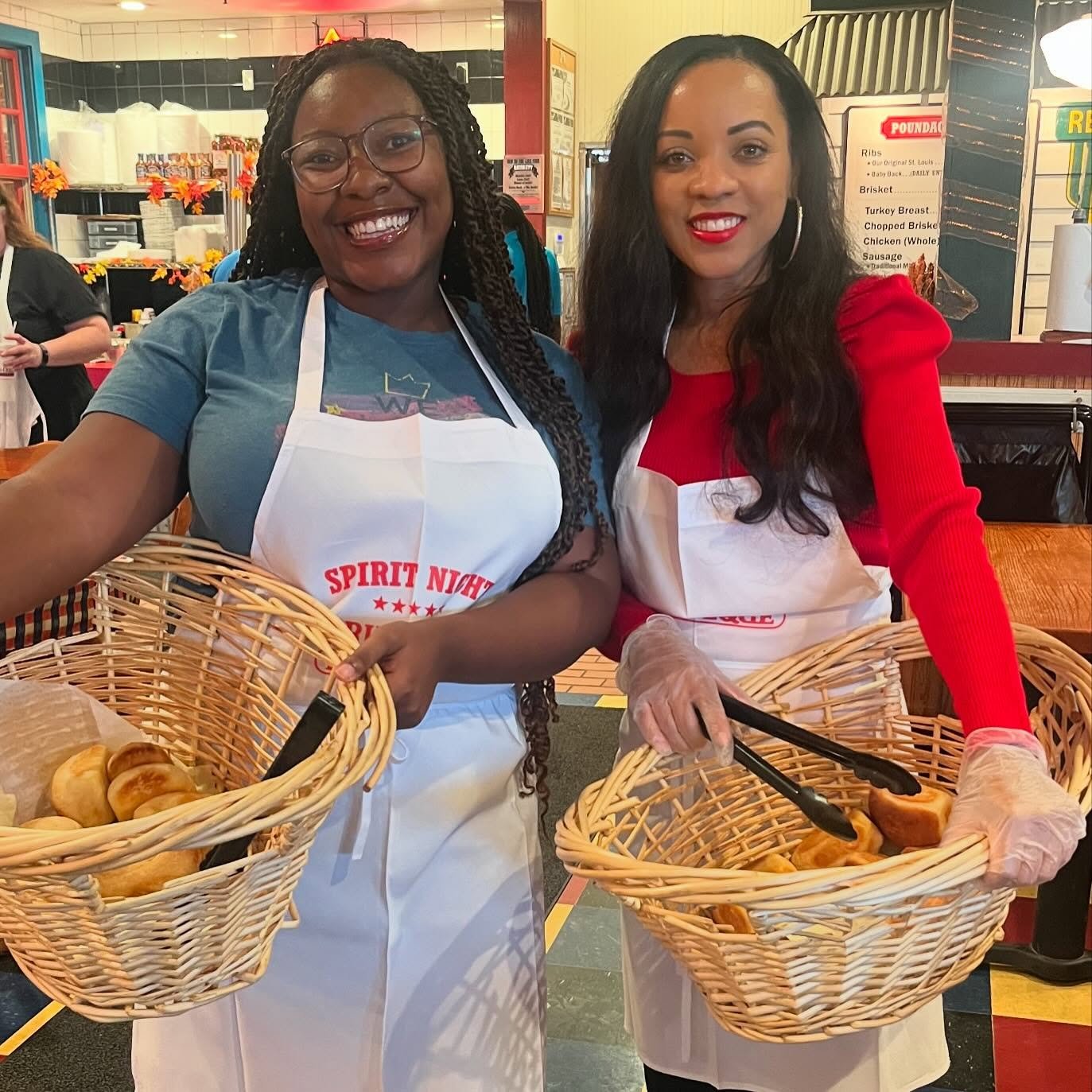Two McNeil teachers smile holding huge baskets of dinner rolls.