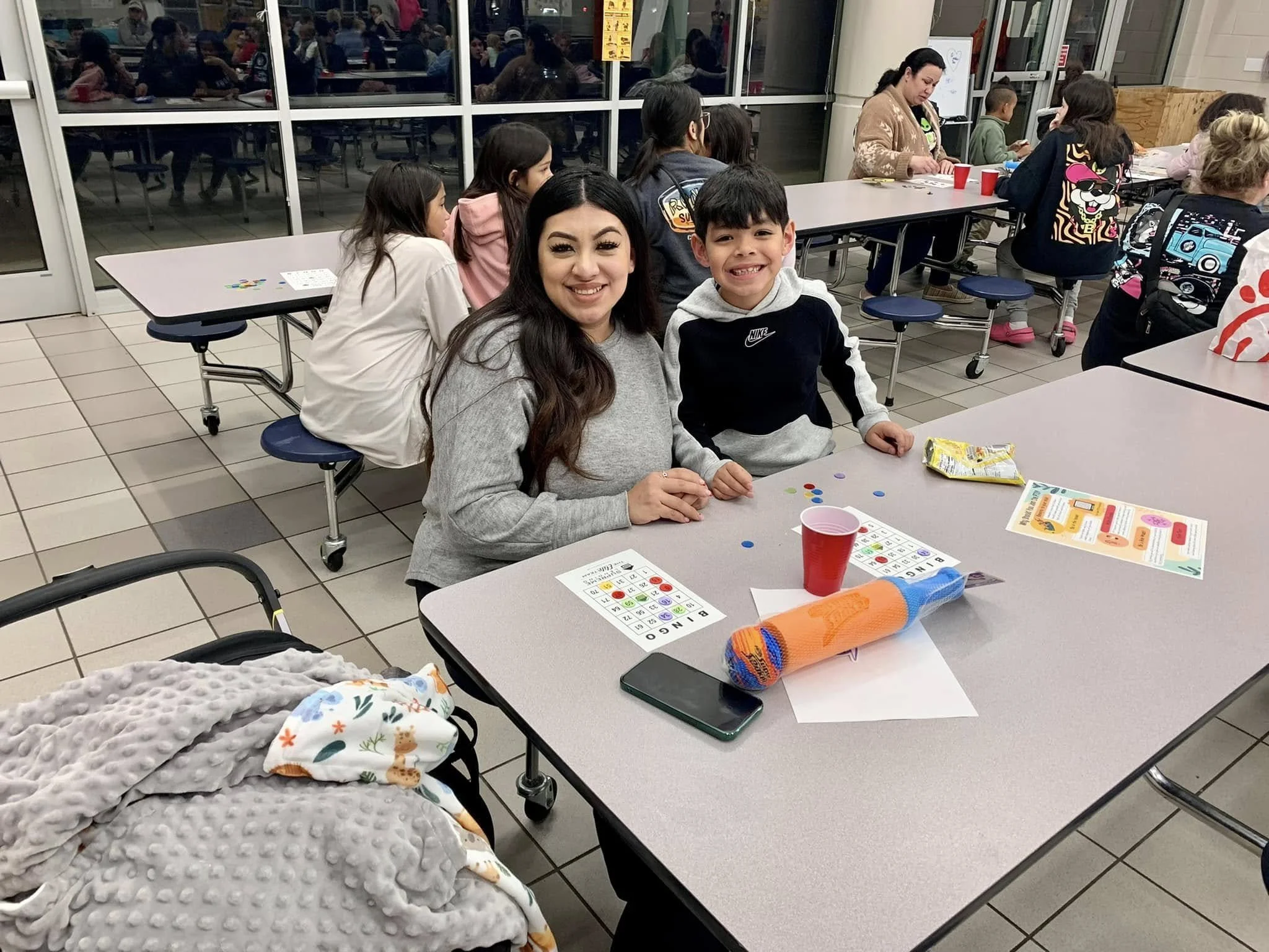 A parent and student seated at a table smile with their Bingo cards.