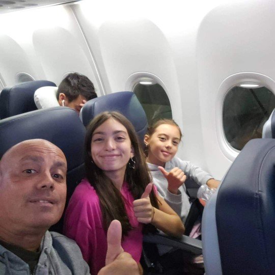 Un grupo de personas en un avión, con dos niñas sonriendo y haciendo gesto de pulgar hacia arriba.