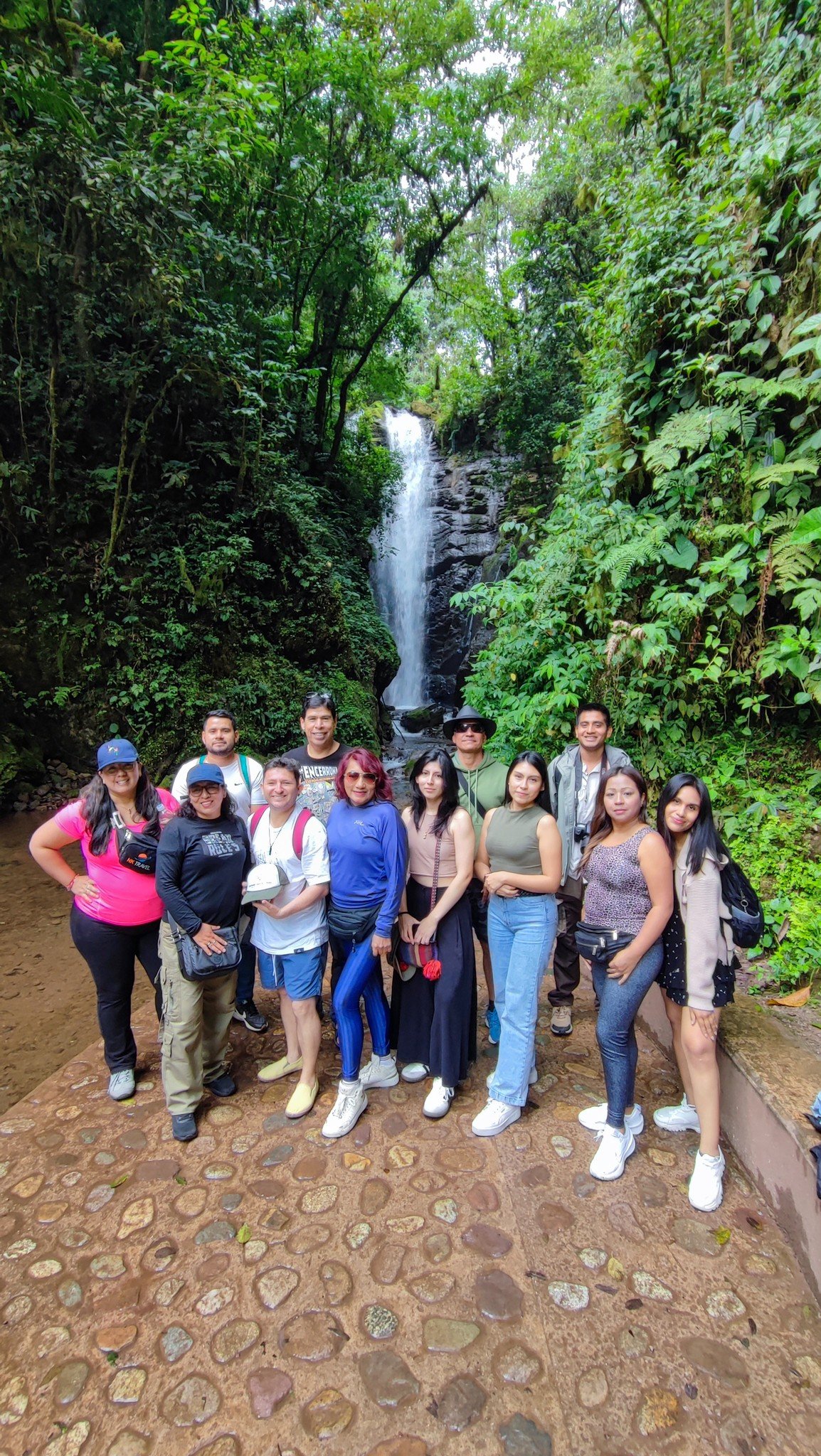 Un grupo de personas de diferentes edades posando frente a una cascada en un entorno selvático.