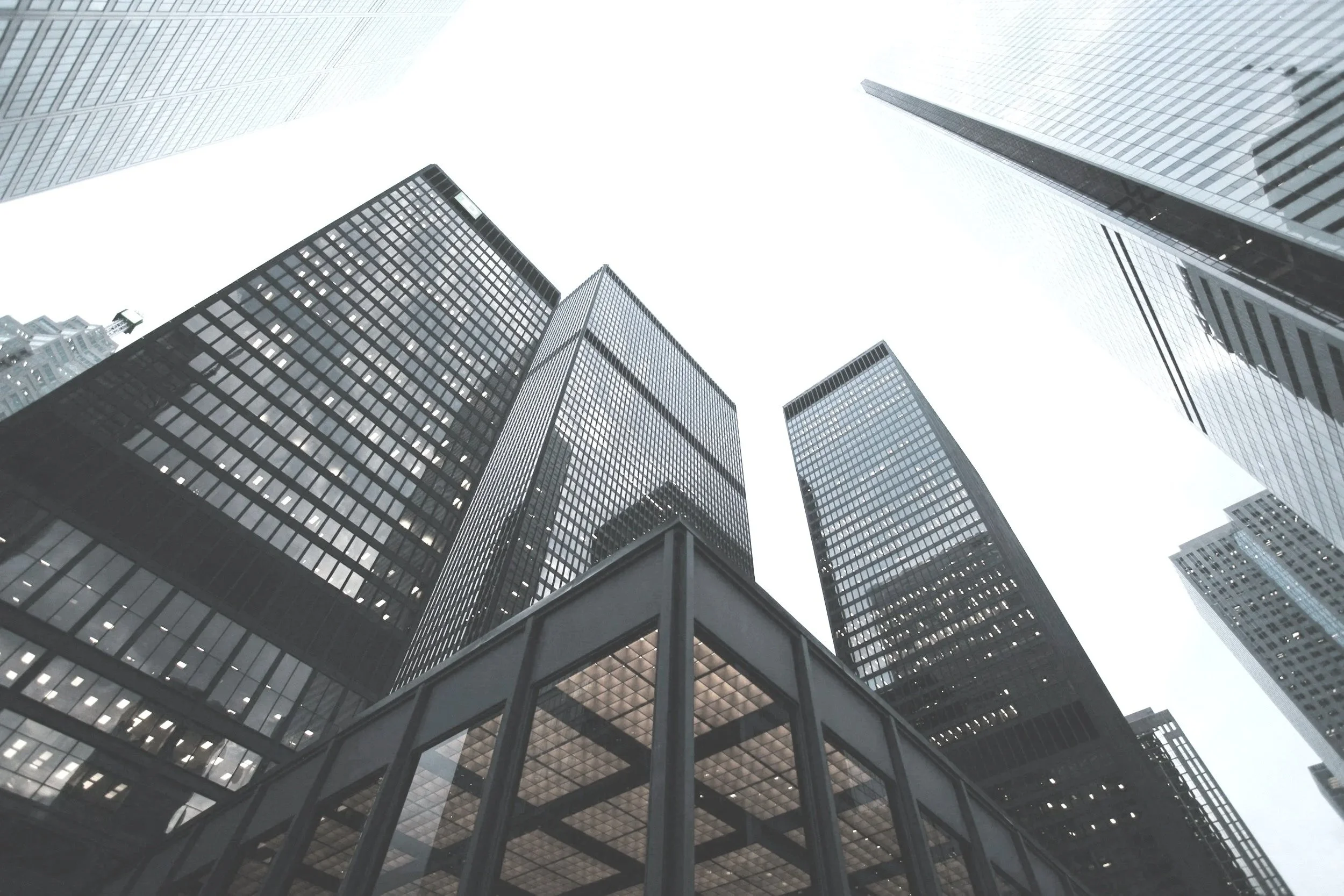 Multiple tall modern office buildings with glass facades viewed from the ground looking up toward the sky.