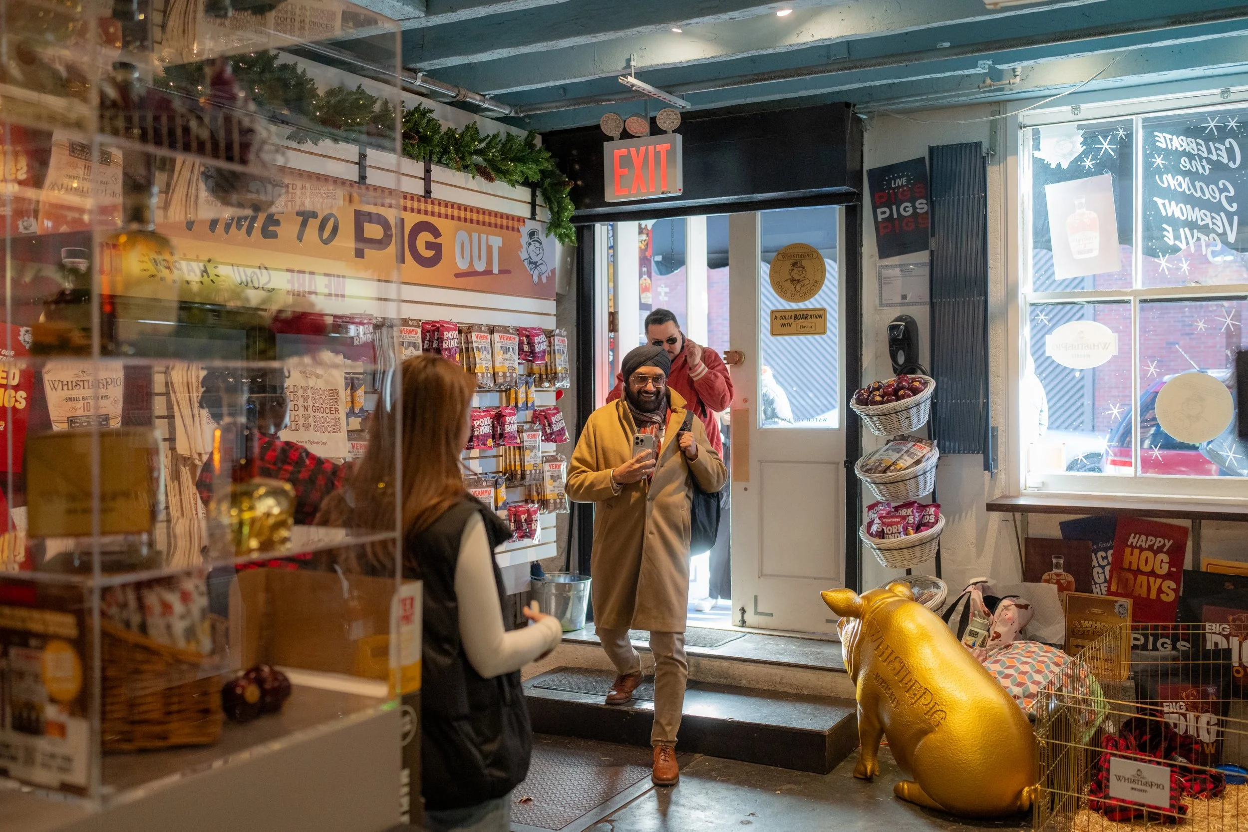 People entering a store decorated for Christmas, with a large sign reading 'Time to PIG Out,' a golden pig statue outside, and holiday-themed decor inside.