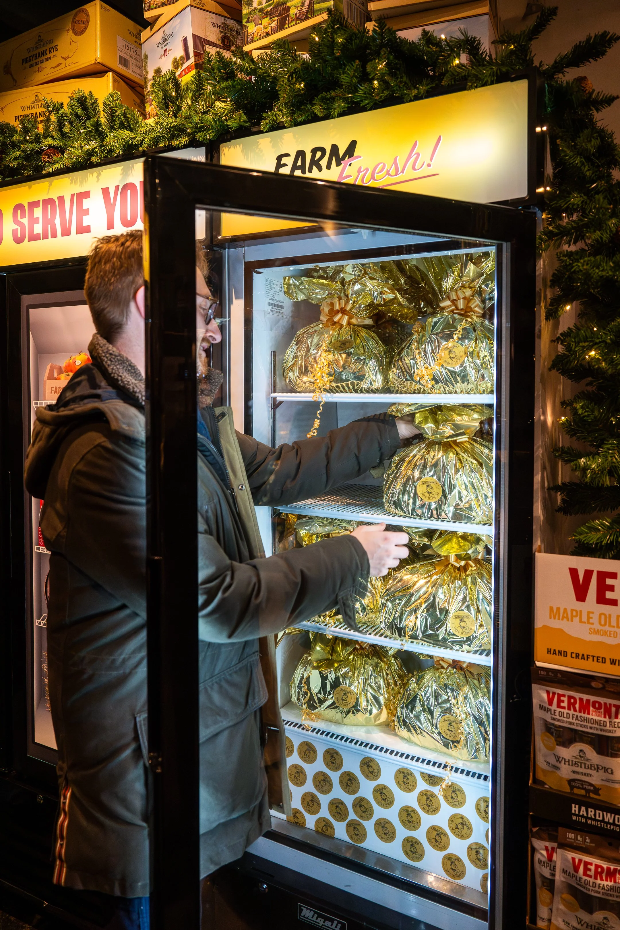 A man shopping for maple syrup in a vending machine wrapped in gold foil, with Christmas decorations around it.