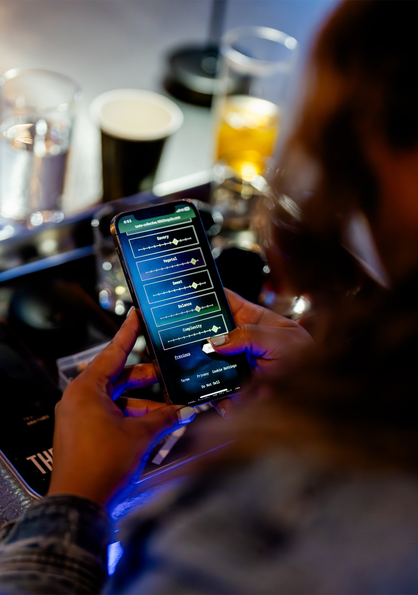 Person holding a smartphone with an app that displays music or audio settings, with drinks and a bar countertop in the background.