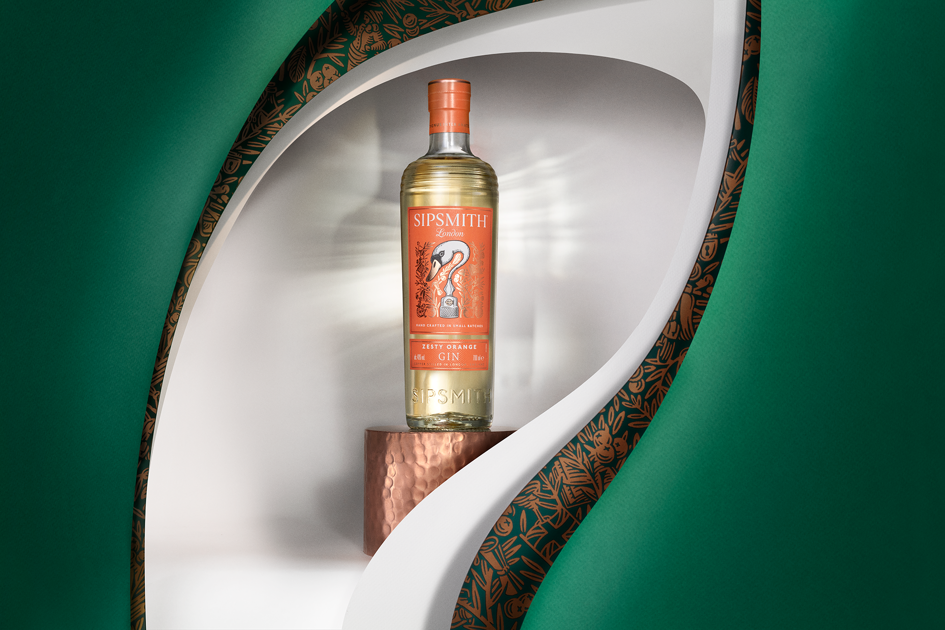 A bottle of Sipsmith London Zesty Orange Gin displayed on a small copper pedestal inside a white niche, framed by a green and patterned black and gold arch.