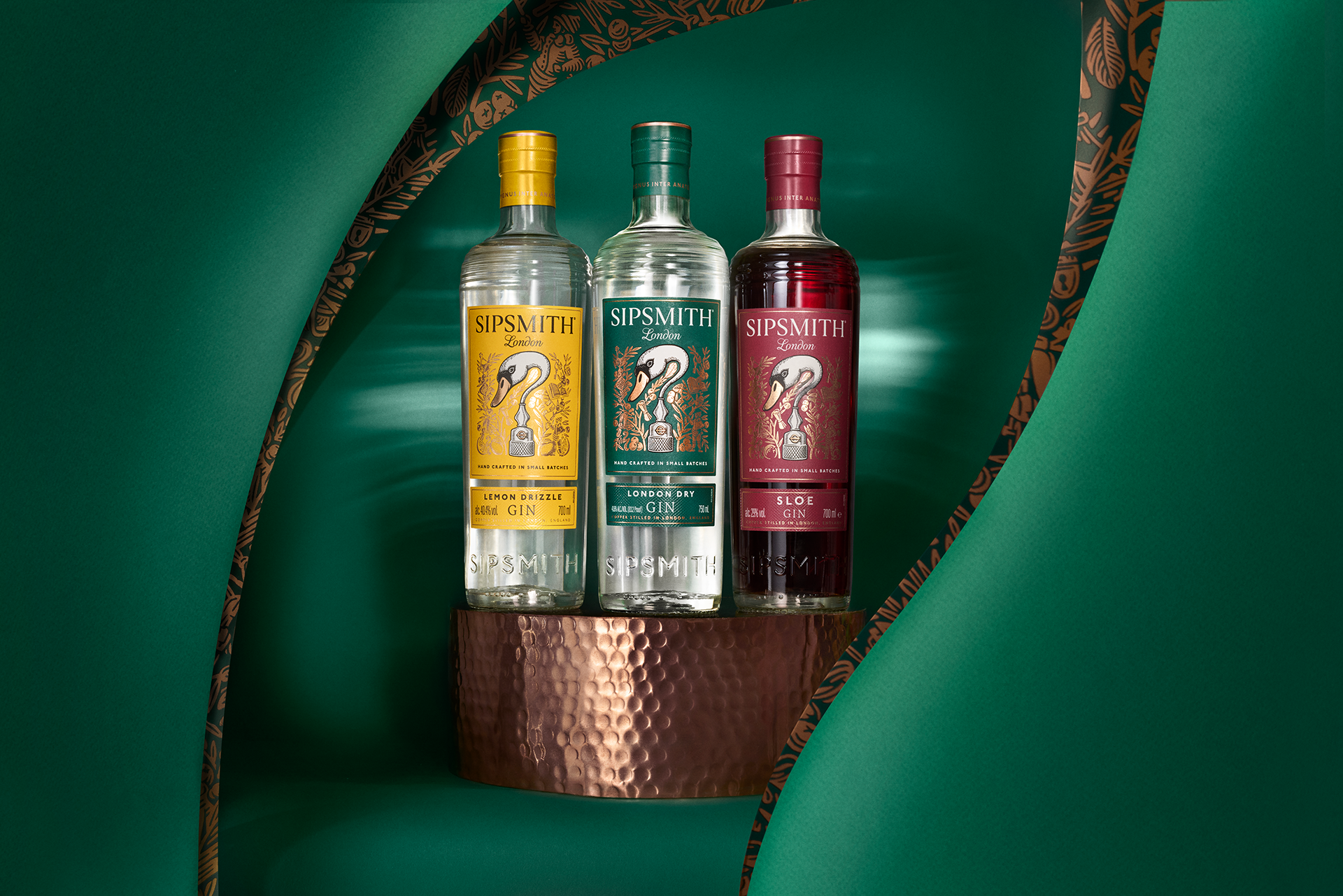 Three bottles of SIPSMITH London gin with different labels—Lemon Drizzle, London Dry, and Sloe—are displayed on a textured copper stand, set against a green background with decorative cutouts.
