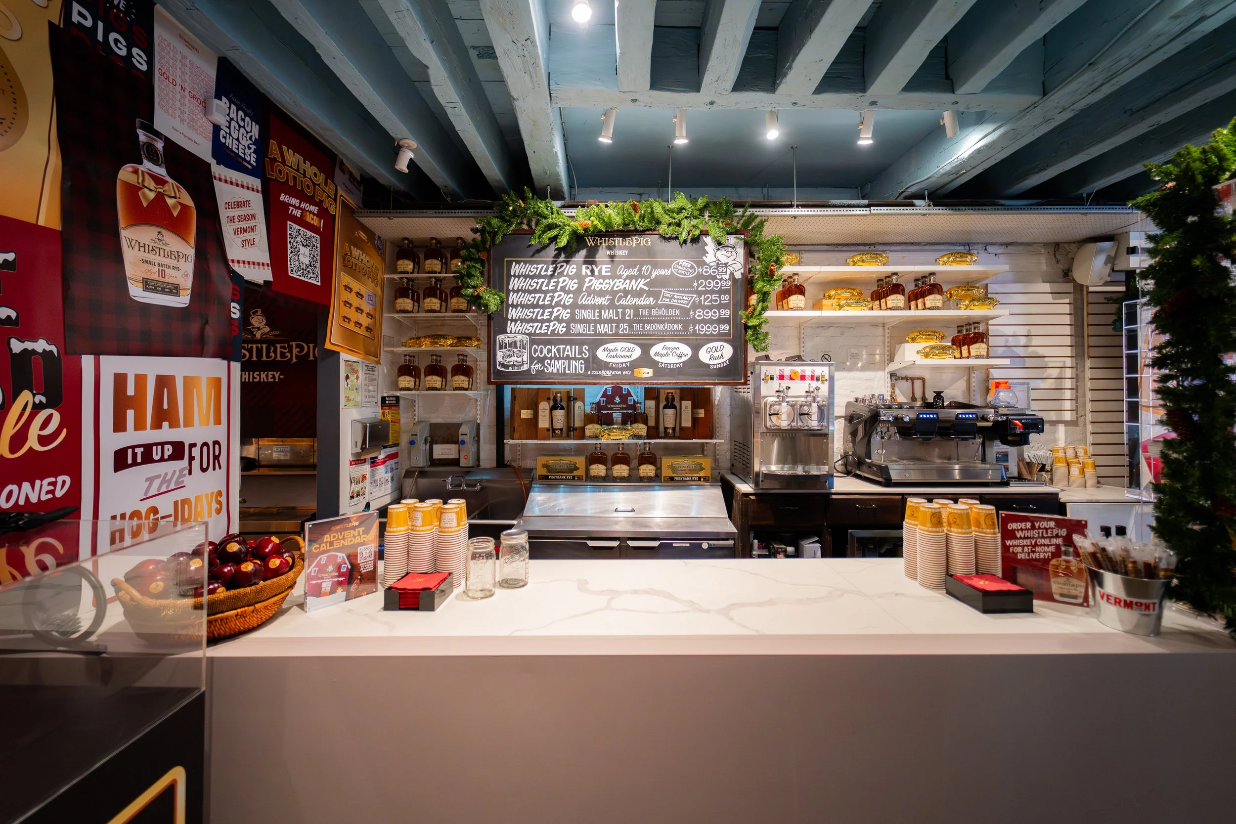 Inside a whisky shop with a white marble counter, bottles of whisky, a chalkboard menu, promotional signs, and a coffee machine.