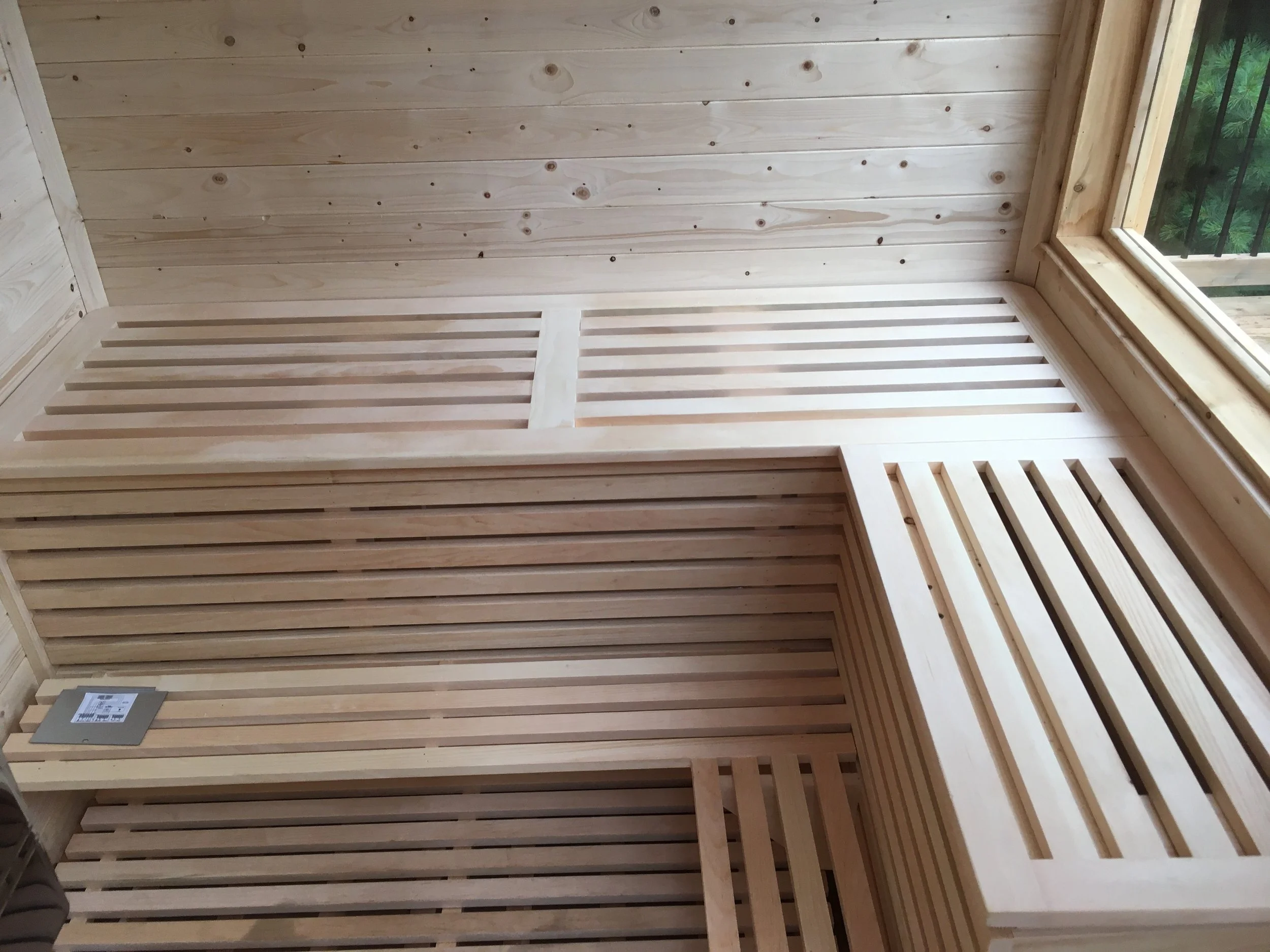Wooden sauna with slatted benches and walls, near a large window overlooking greenery.
