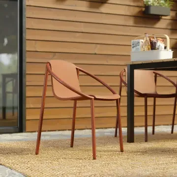 Outdoor patio scene with two pink chairs and a table against a wooden wall