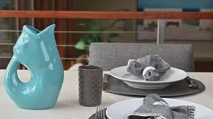Table setting with a turquoise vase, a gray candle holder, two plates with gray napkins, and a gray decorative object on a gray placemat.