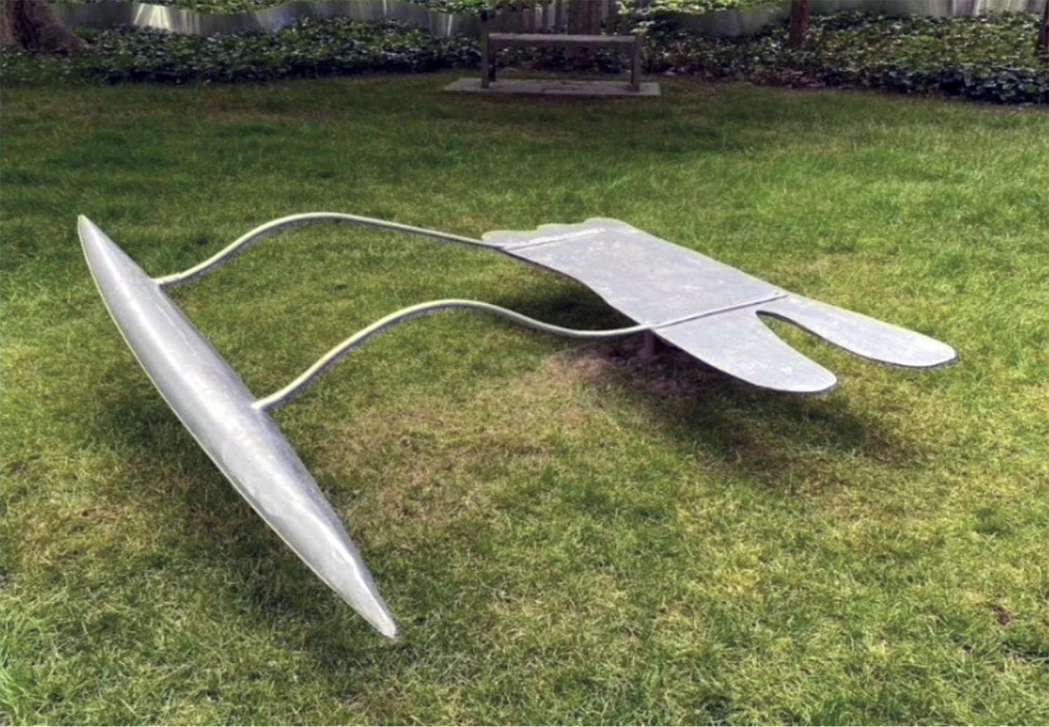 Metal lawn chair resembling a rocket, with a curved body and fins, placed on grass in a garden.