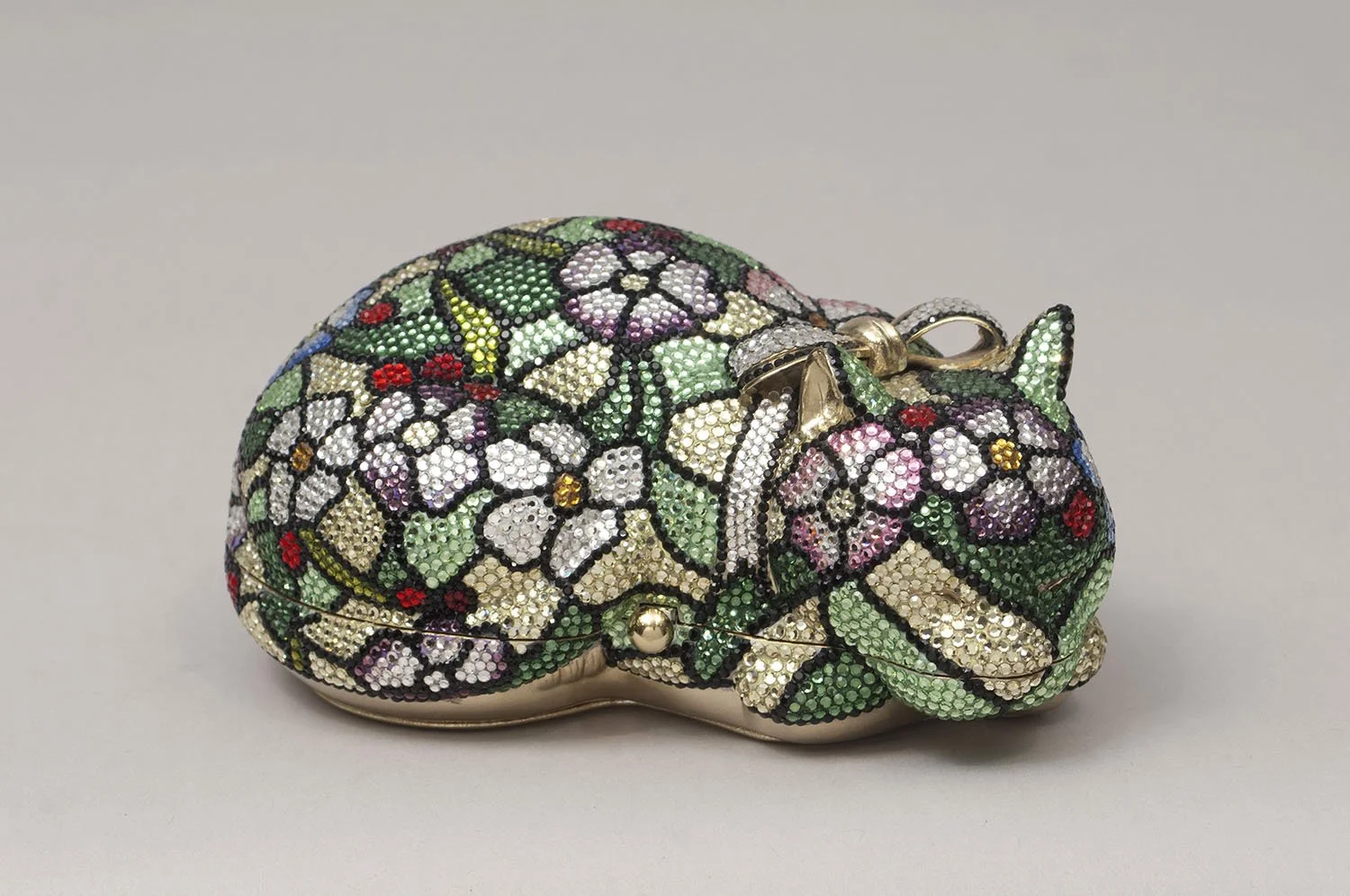 A decorative purse shaped like a cat covered in multicolored rhinestones and floral patterns.
