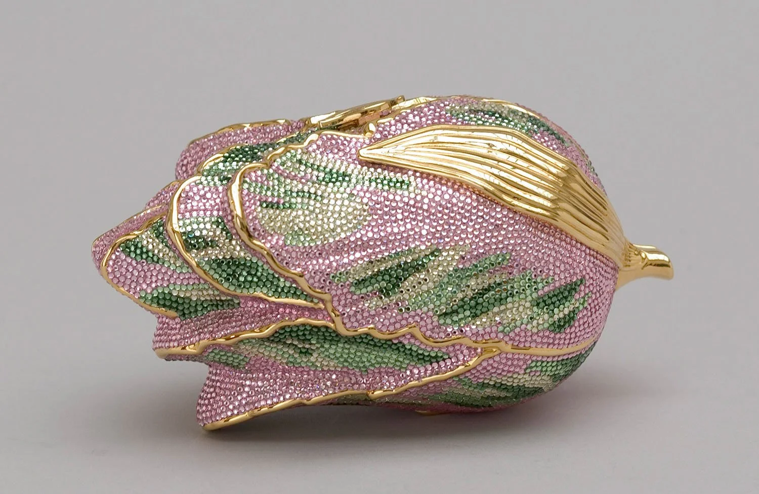 A decorative flower-shaped brooch with pink, green, and gold colors, adorned with rhinestones and intricate gold accents.