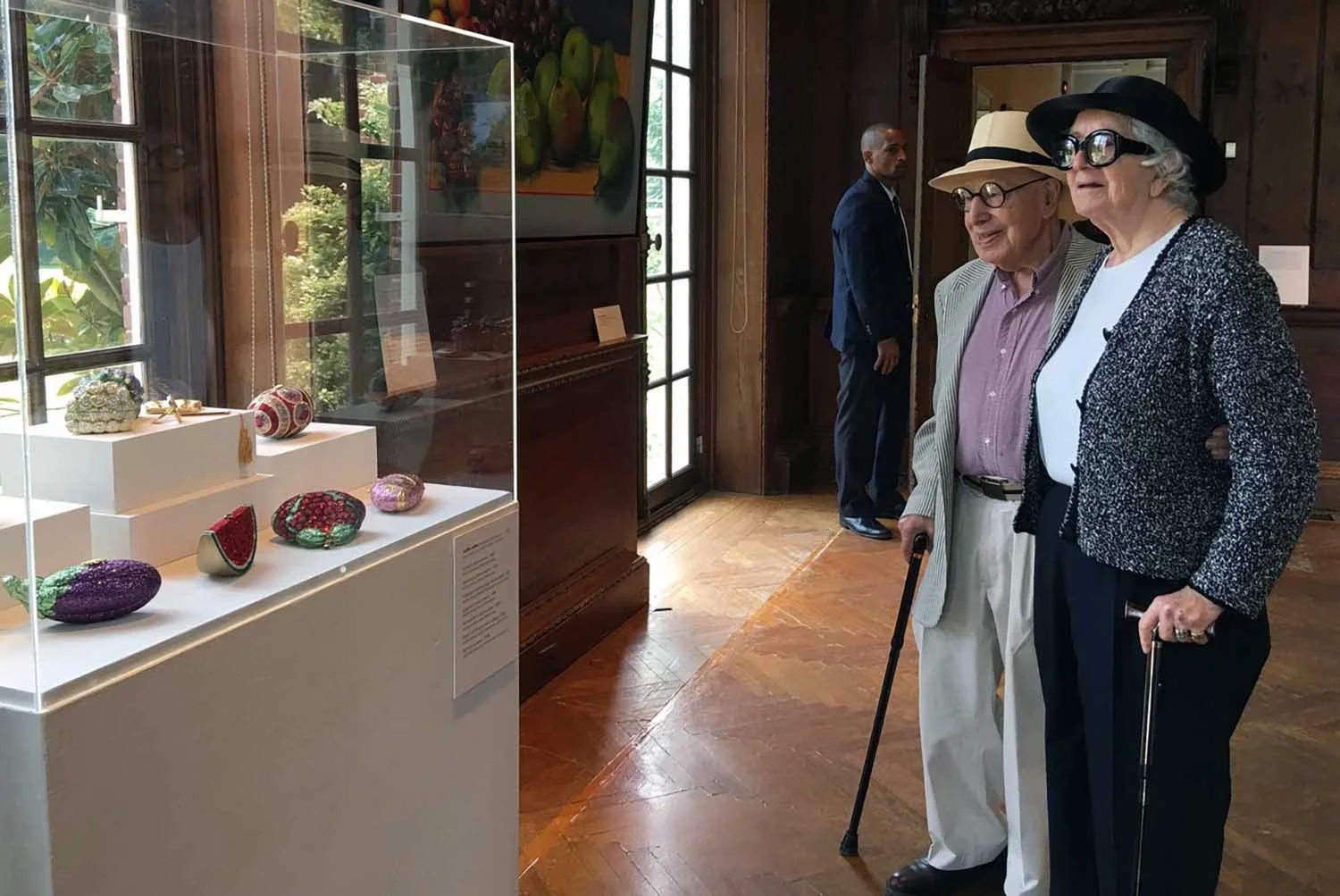 Black and white photo of Gerson Leiber and Judith Leiber facing each other, both wearing round glasses and straw hats, against a plain white background.