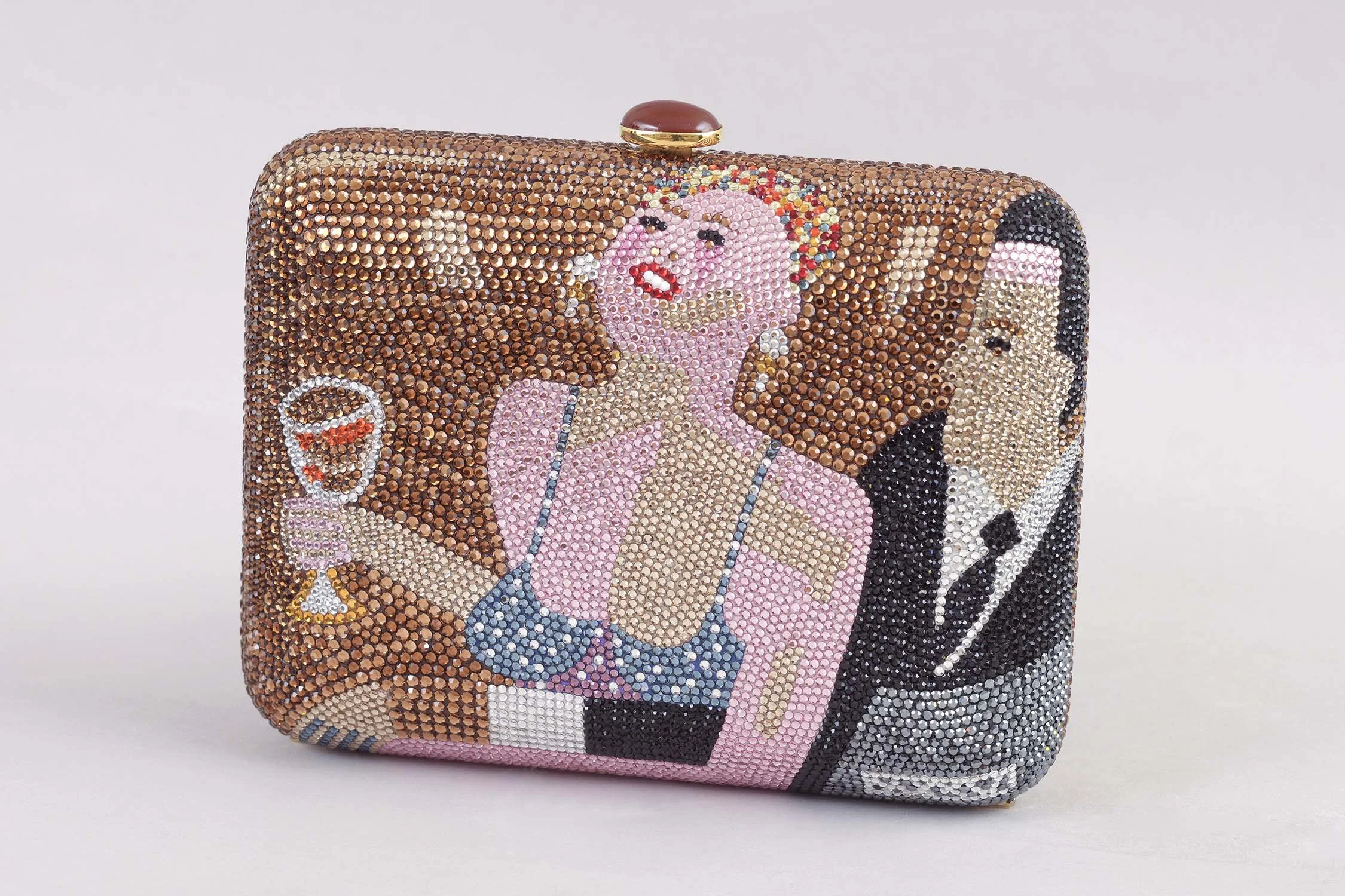 A rectangular clutch purse by famed handbag designer Judith Leiber decorated with rhinestones featuring a cartoon-style image of a woman with pink hair, a drink, and a man in a tuxedo, all outlined with rhinestones.