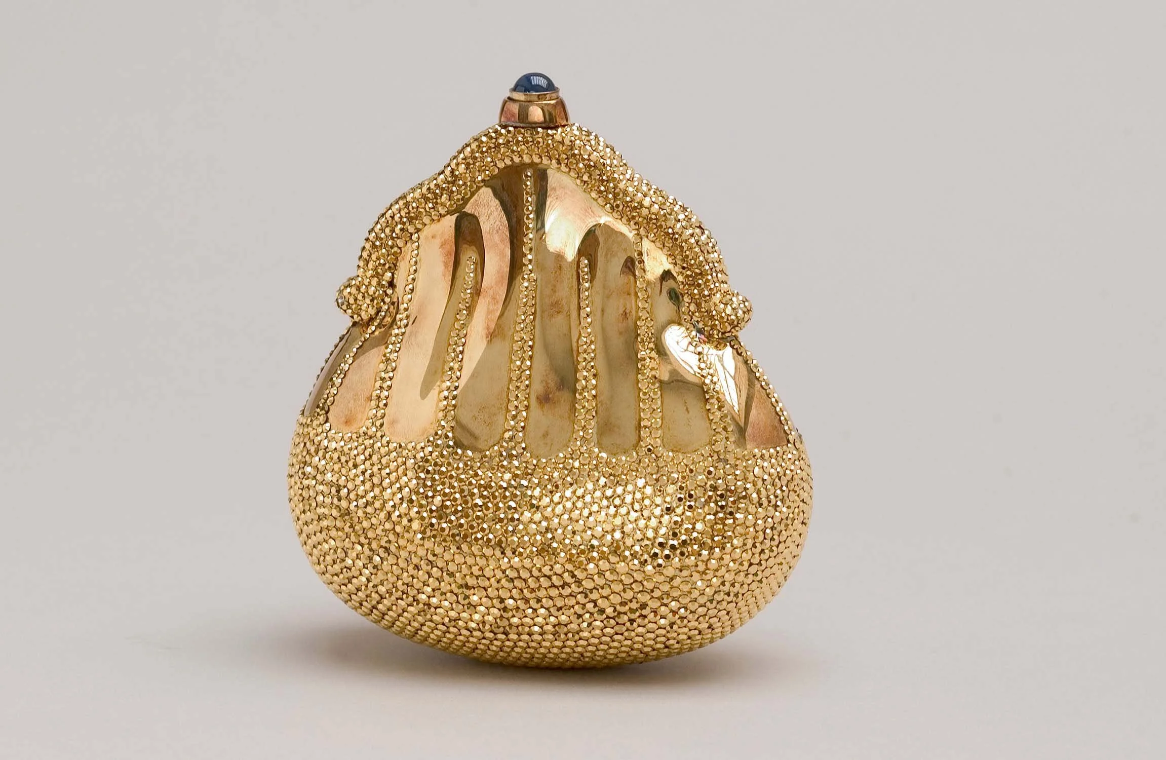 A Judith Leiber handbag designed to look like a pearl oyster with a pearl inside, embellished with gold studs and a gold chain-like strap.