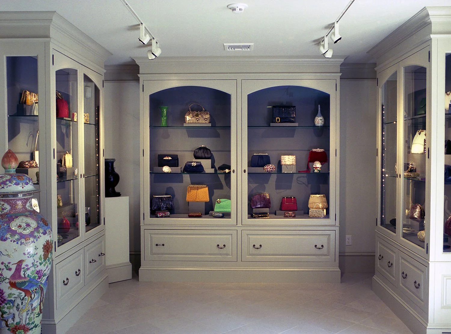A display of various handbags inside a white wooden showcase with glass doors in a store.