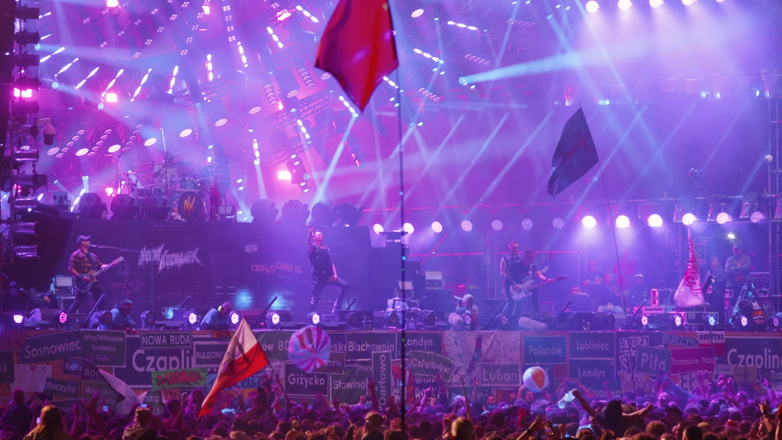 piosenkarz an scenie podczas festiwalu muzycznego trzyma rękę podniesioną do góry. W ręce trzyma mikrofon.