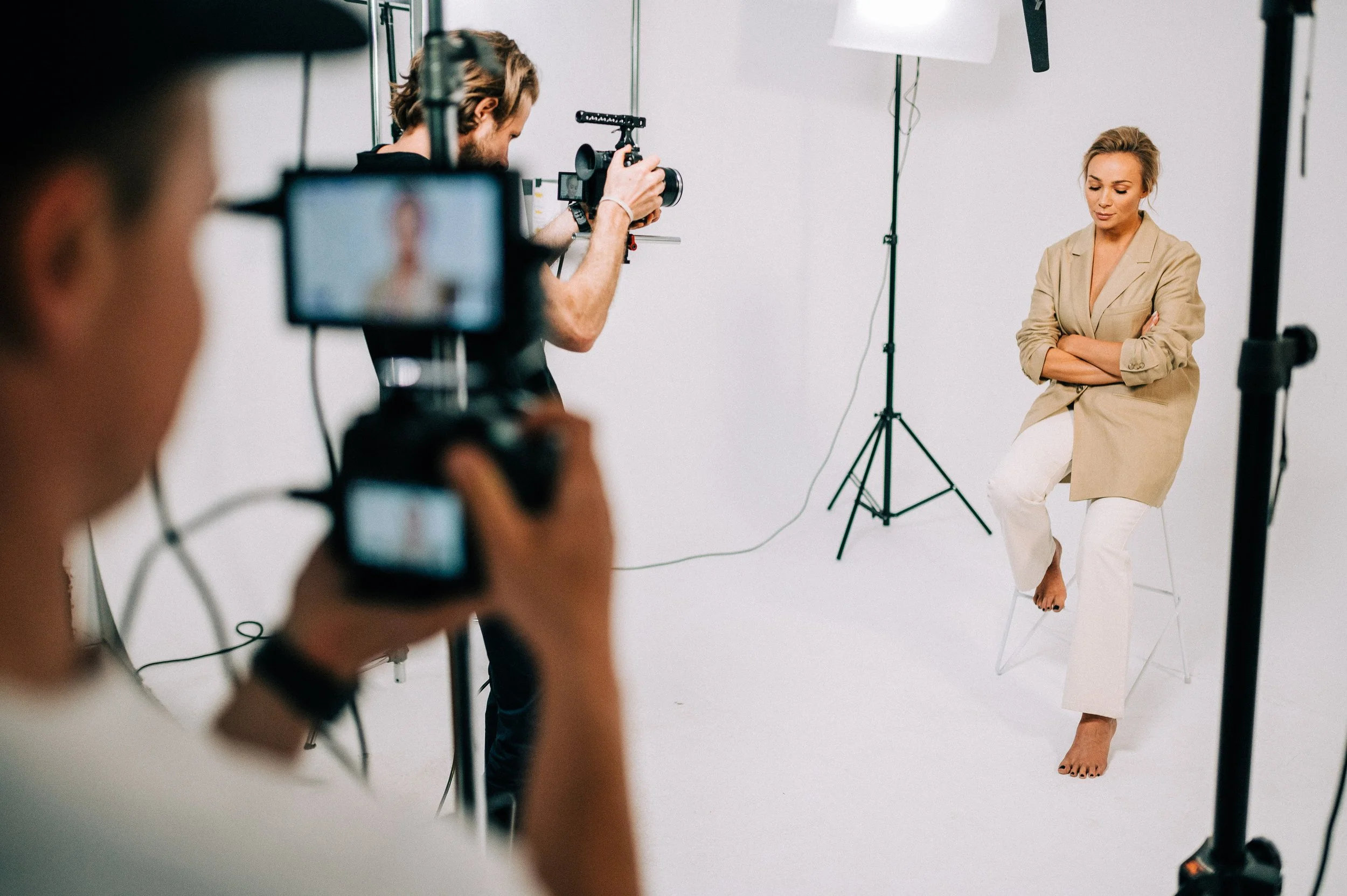 Kobieta siedzi na krześle w studio filmowym, dwaj mężczyźni z kamerami ją nagrywają.