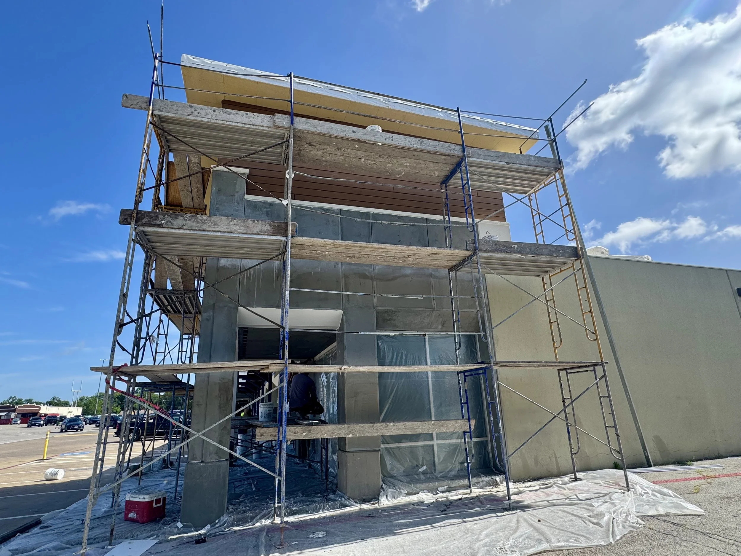 Under construction building with scaffolding and a worker installing a window during daytime.