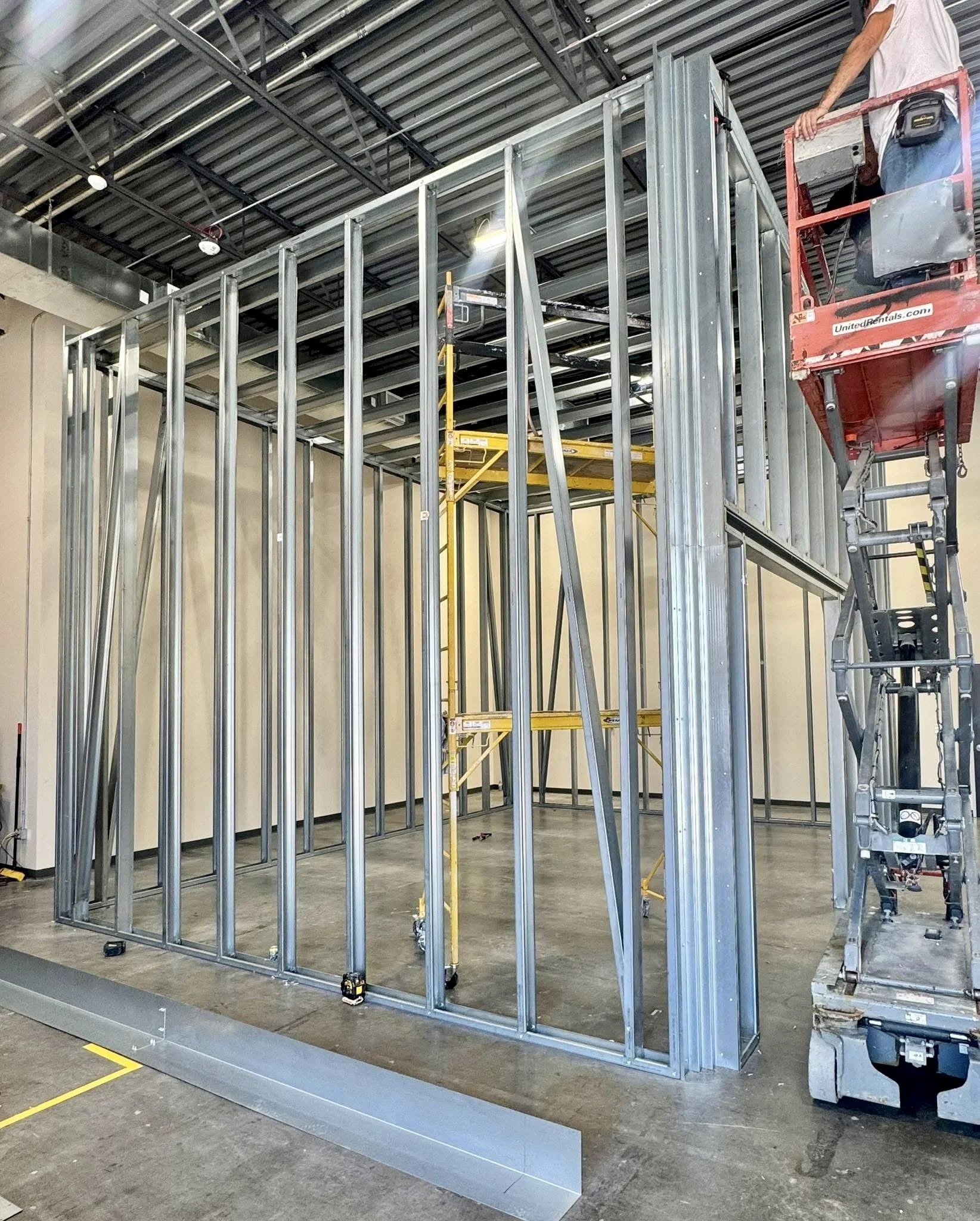 Metal framing for a building under construction with a worker on a lift in an industrial space.