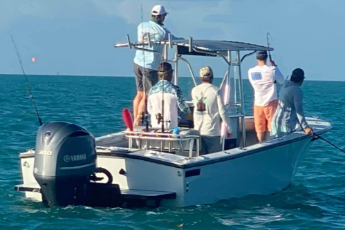 Group of five men on a small motorboat fishing in the ocean, with one man standing at the front and others sitting or standing near the center.