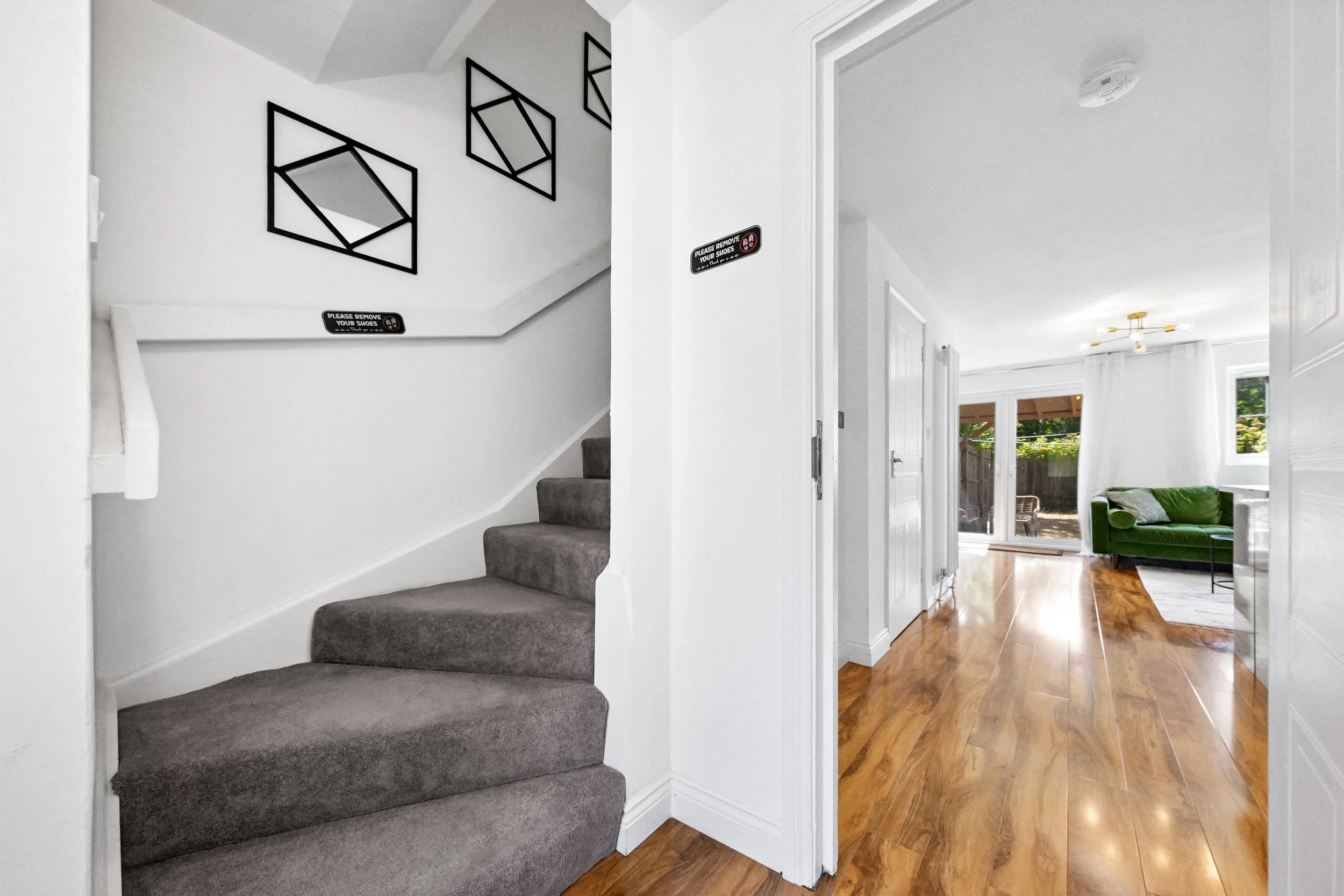 Interior view of a home with a carpeted staircase on the left and a living room with hardwood floors, a green couch, and large sliding glass doors leading outside on the right.