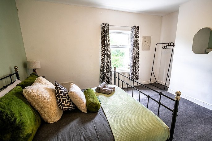 Bedroom with a bed, pillows, curtains, a window, and a clothes rack.