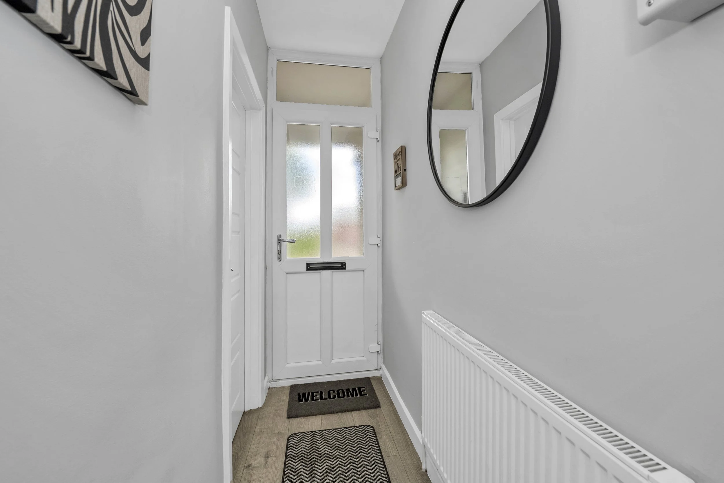 Entryway with a white front door, a round mirror on the right wall, a welcome doormat, and a radiator along the right wall.