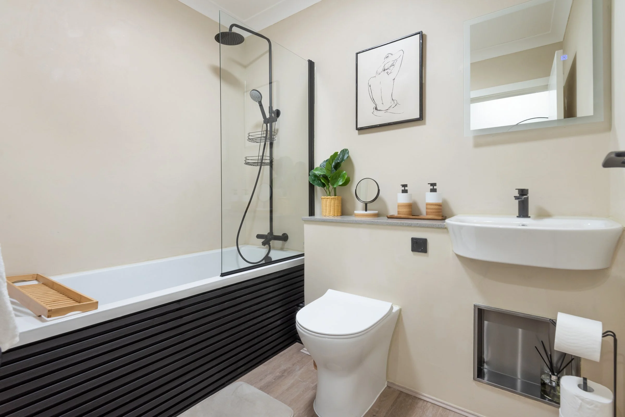 Modern bathroom with bathtub, walk-in shower, toilet, and small sink, decorated with minimalistic art and green plant.