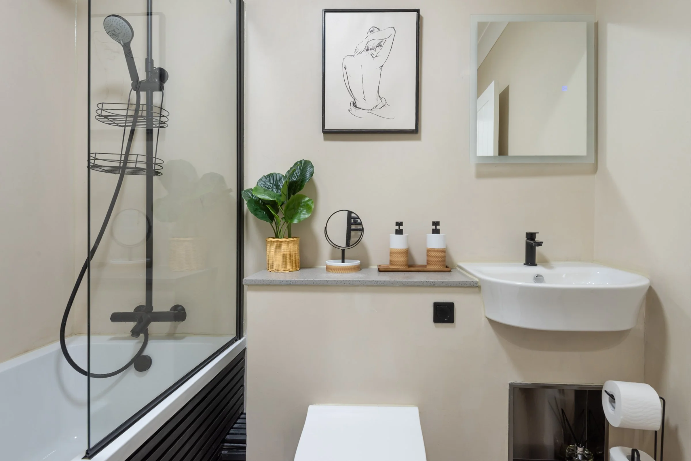 Modern bathroom with walk-in shower, white wall with artwork, mirror, small sink, potted plant, soap dispensers, mirror, and toilet paper holder.