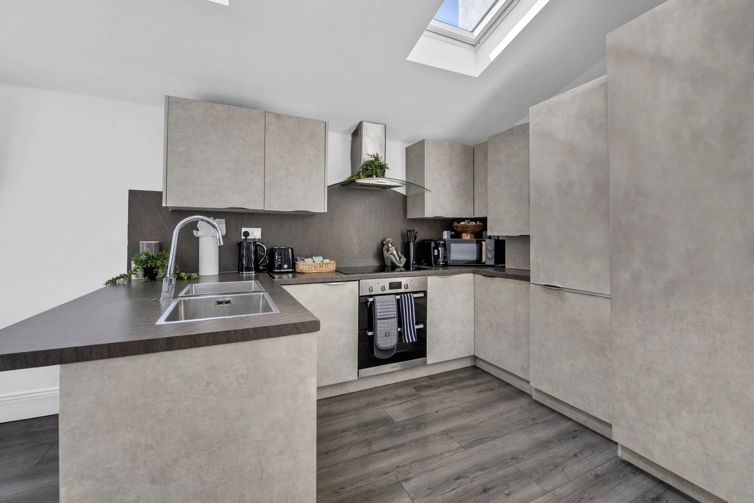 Modern kitchen with beige cabinets, dark countertops, microwave, toaster, kettle, and a skylight.