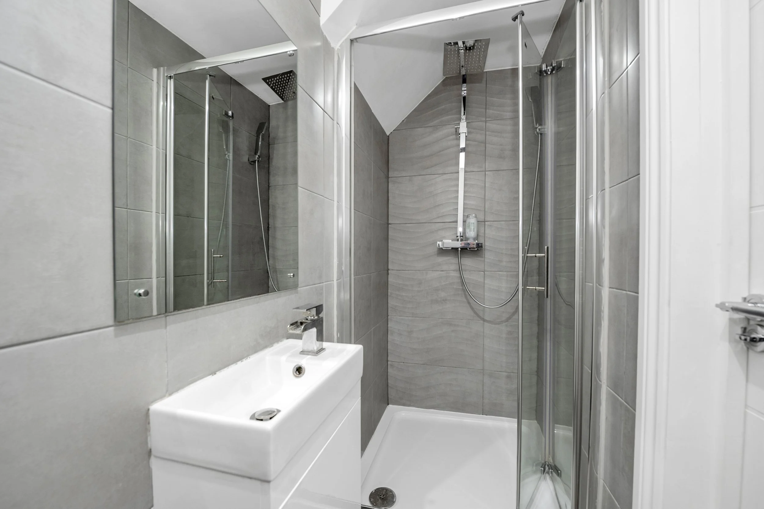 Small modern bathroom featuring a corner shower with glass doors, a wall-mounted mirror, and a white rectangular sink.