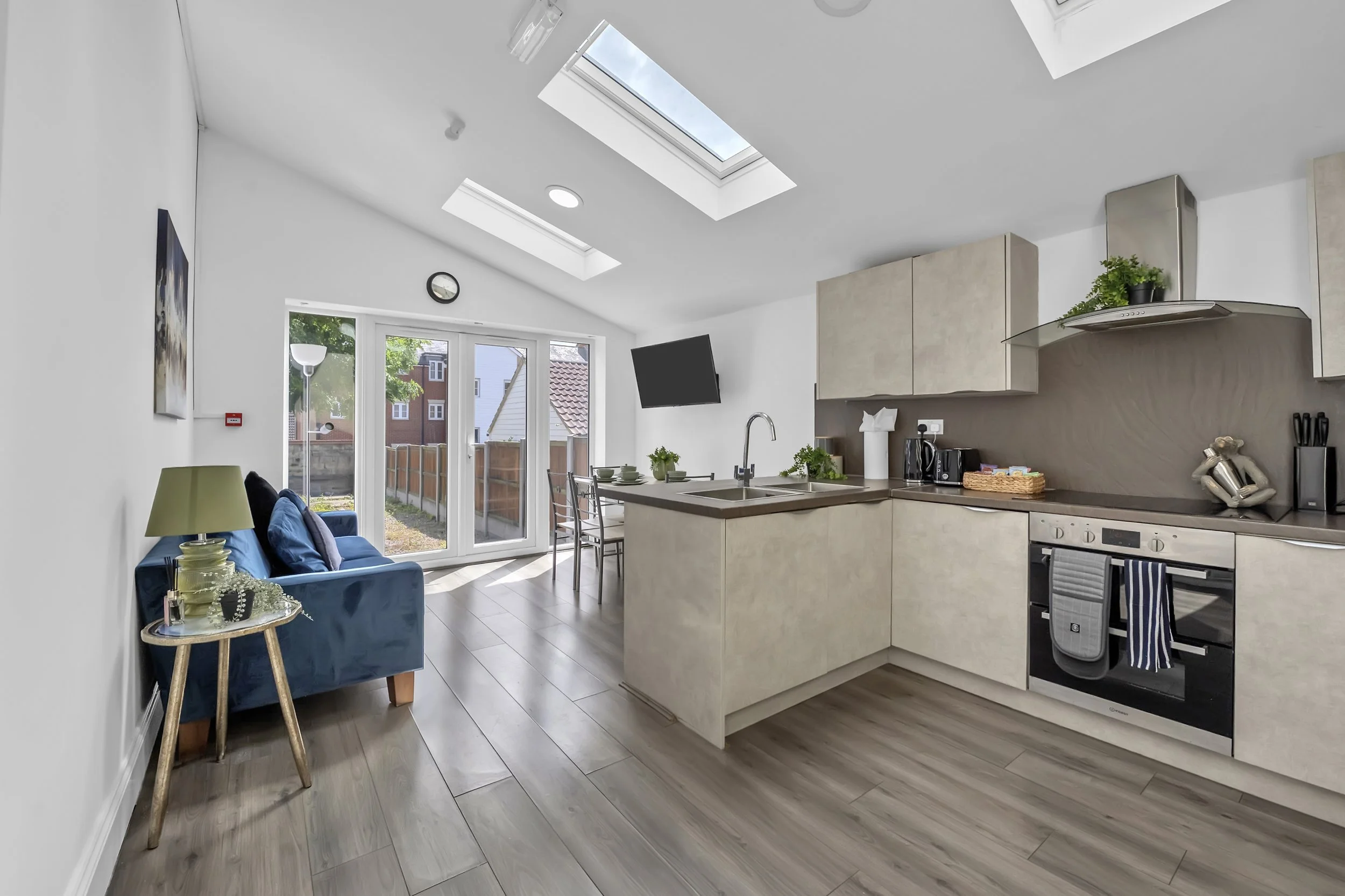 Bright kitchen and dining area with skylights, a sliding glass door leading to a backyard, beige cabinets, and a small living space with a blue sofa and side table.