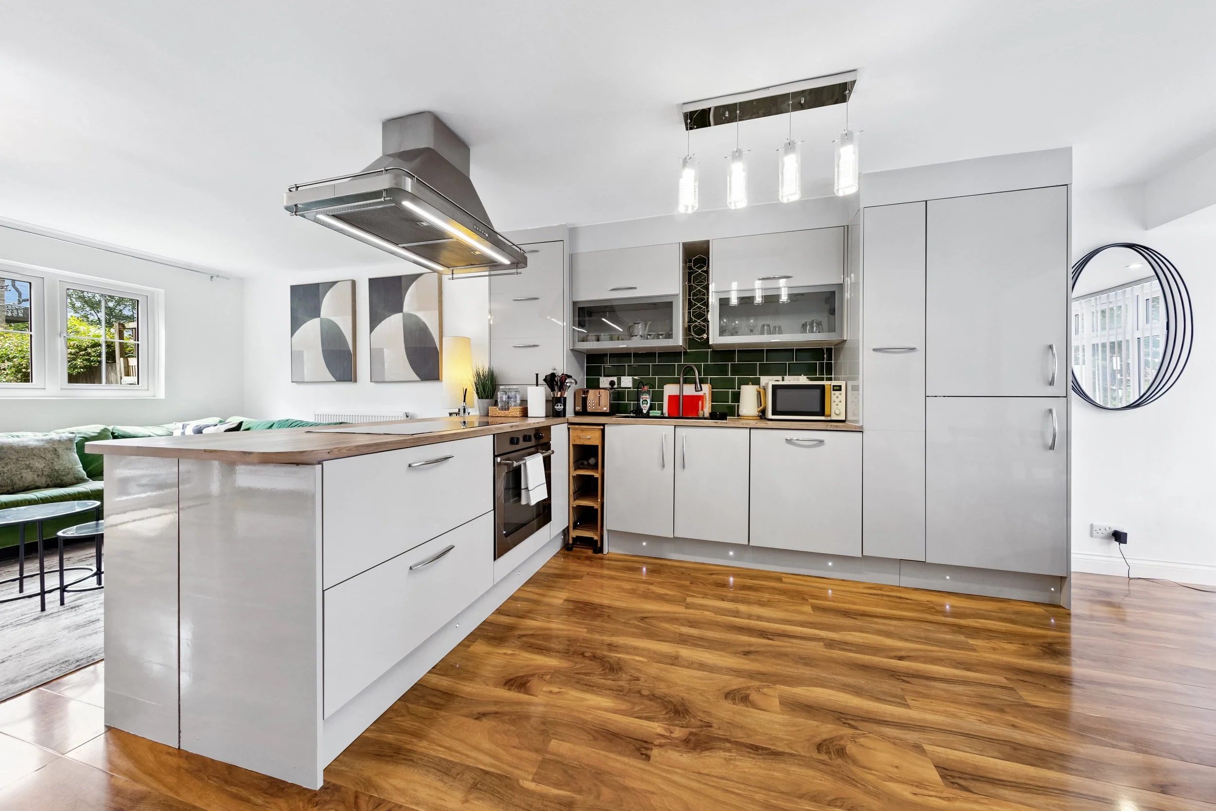 Modern kitchen with white cabinets, wooden floor, green tile backsplash, and stainless steel appliances.