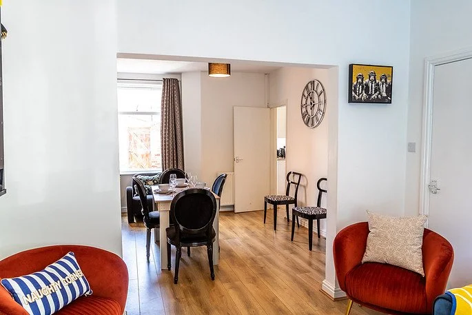 Living room with red armchairs, a dining table with black chairs, and artwork on the walls.