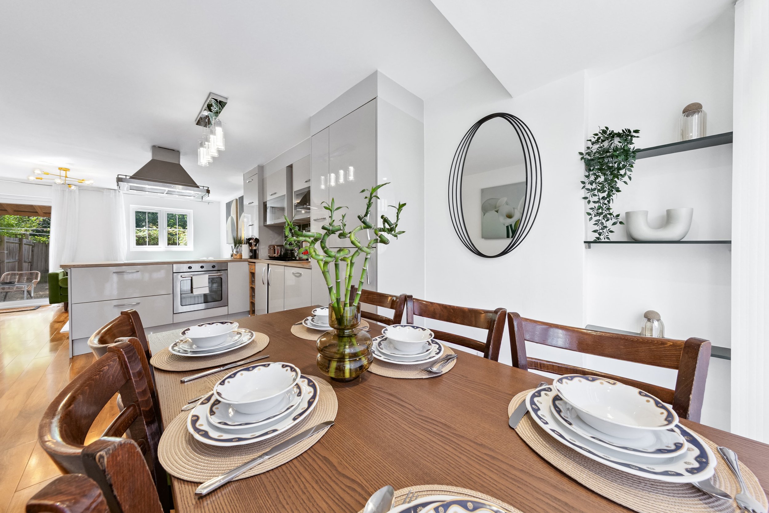 Dining table set with white and navy patterned dishes, silverware, and a central glass vase with green bamboo stalks in a bright, modern kitchen and dining area.