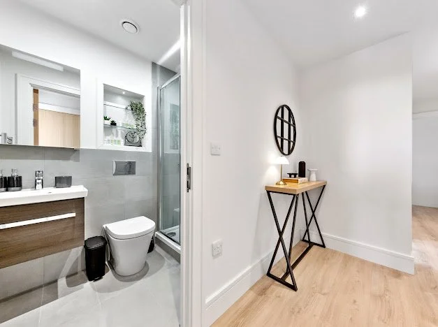Modern bathroom and hallway with a small table decorated with a lamp and oval mirror.
