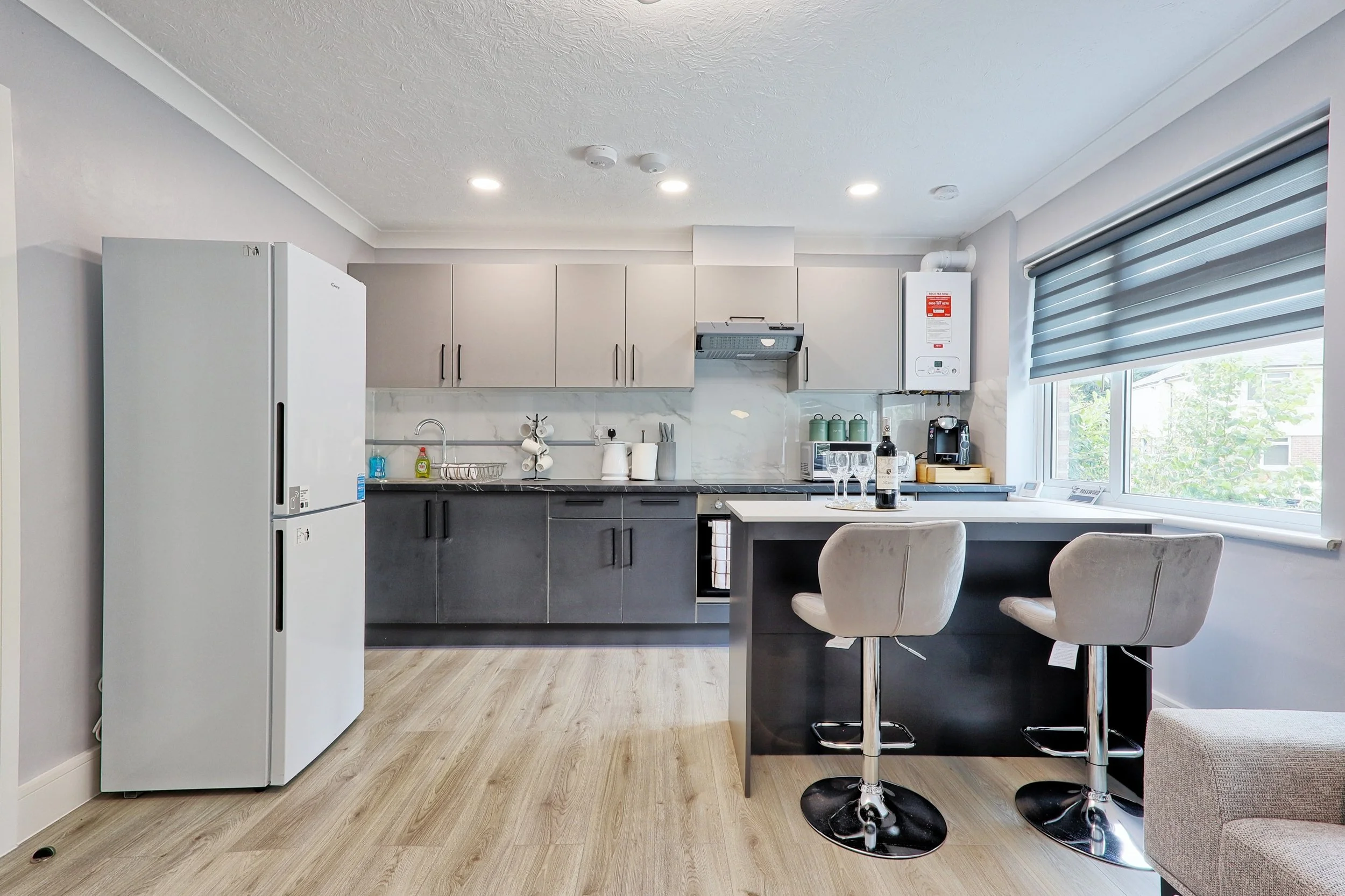 Modern kitchen with white and black cabinets, a refrigerator, a window with blinds, and a kitchen island with two bar stools.