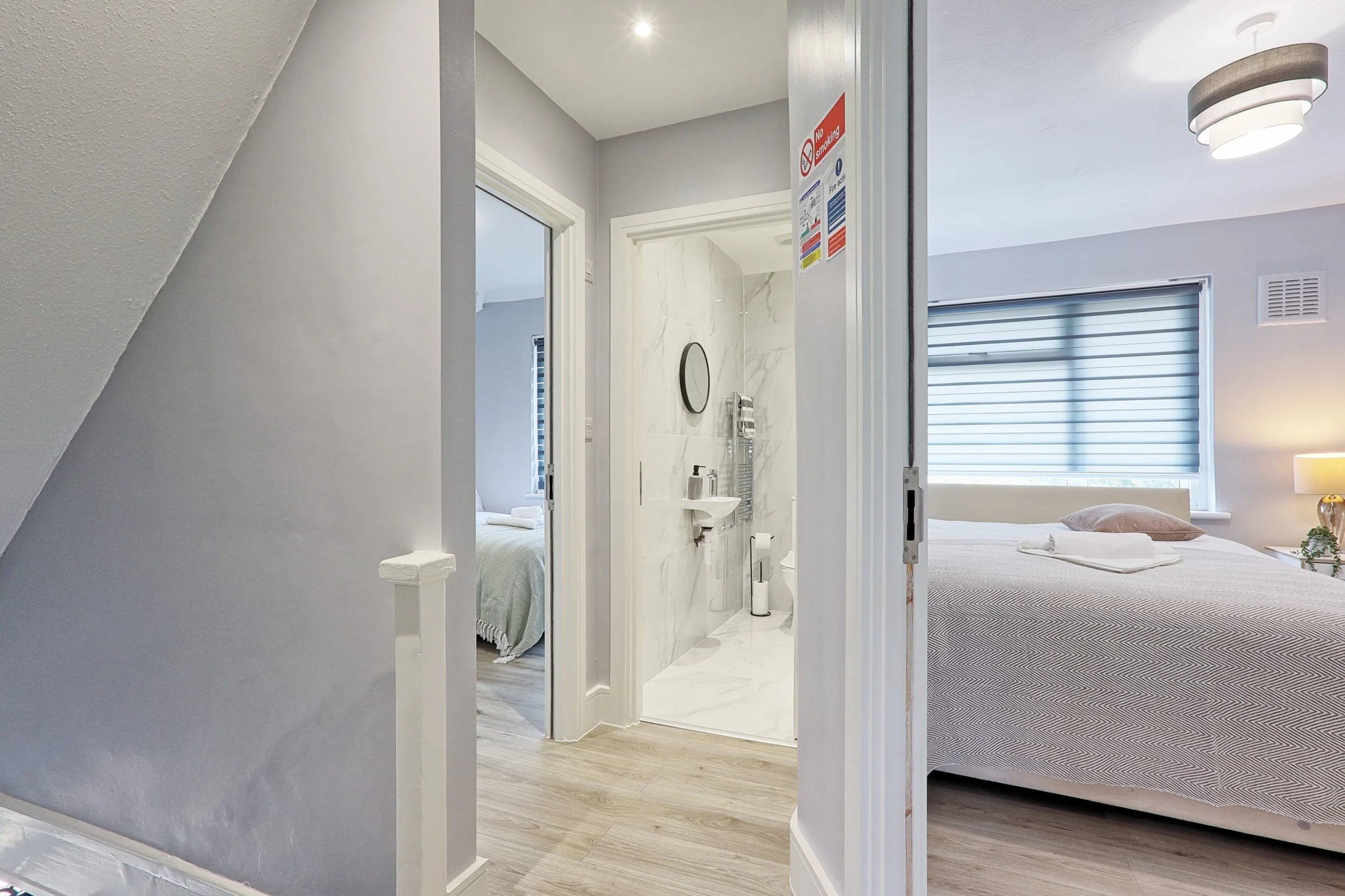 View of a hallway with two bedrooms and a bathroom in a modern home or hotel room, with light-colored walls, wooden floors, and natural lighting.