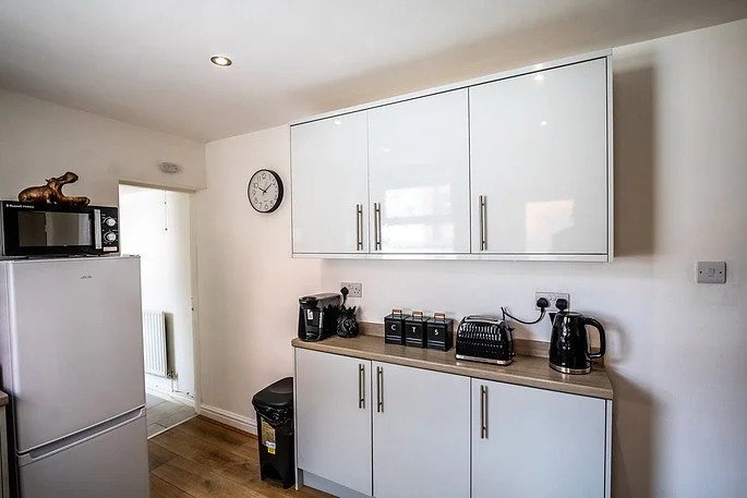Kitchen with white cabinets, toaster, kettle, coffee machine, and a clock on the wall.