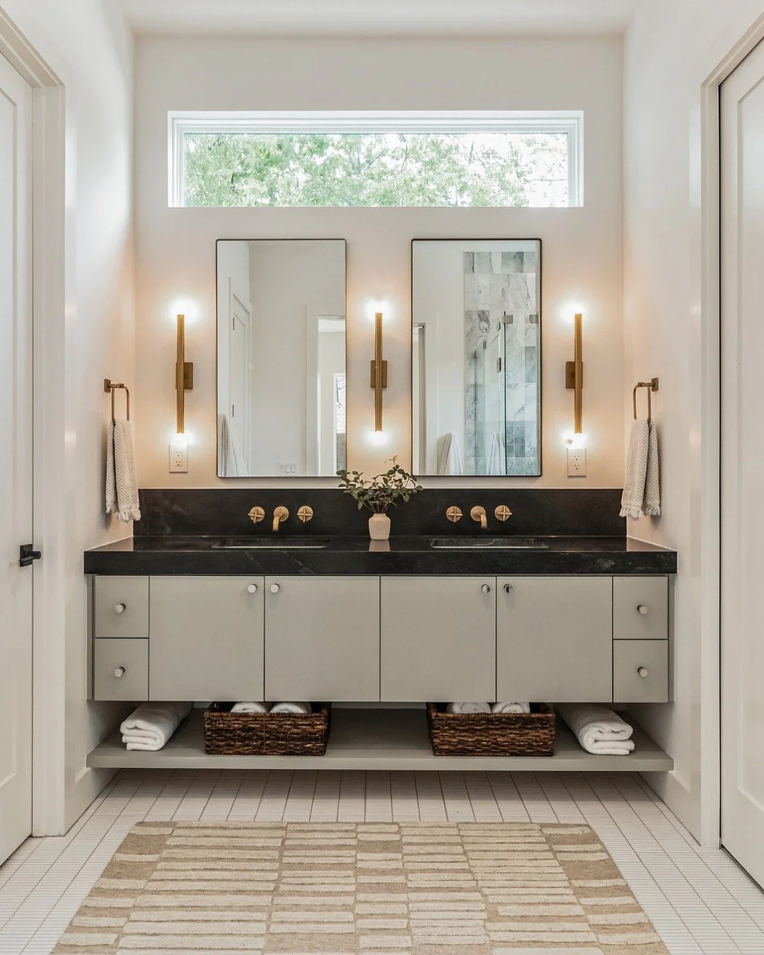 Good lighting makes all the difference.
This bathroom pairs natural light with soft, vertical sconces to keep faces evenly lit. 

Pro Tip: To create a spa-like feel in your bathroom, keep lighting soft, layered, and warm. Combine dimmable sconces or 