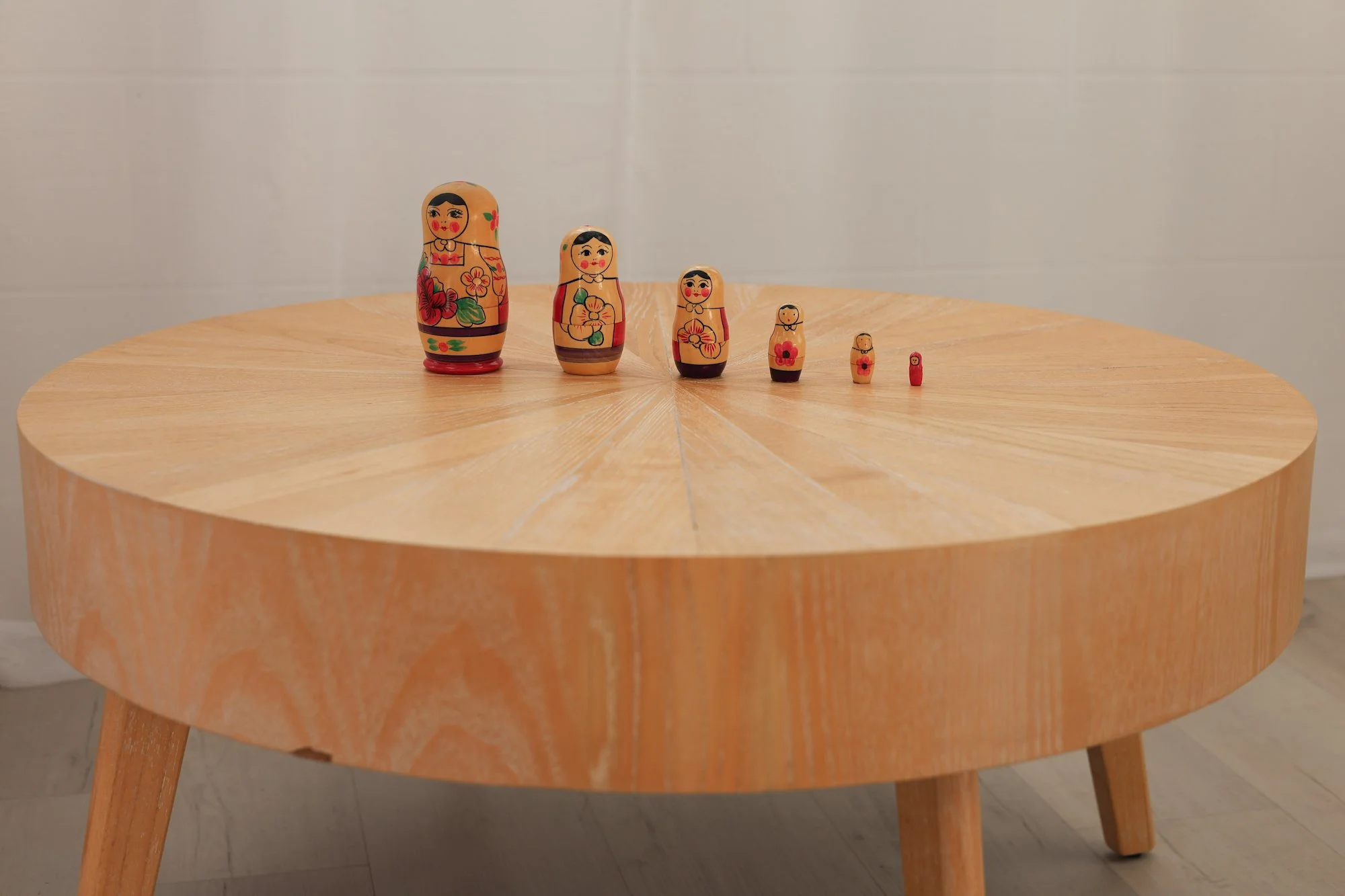 A set of six Russian nesting dolls, decreasing in size from left to right, arranged on a round wooden table with a light background.